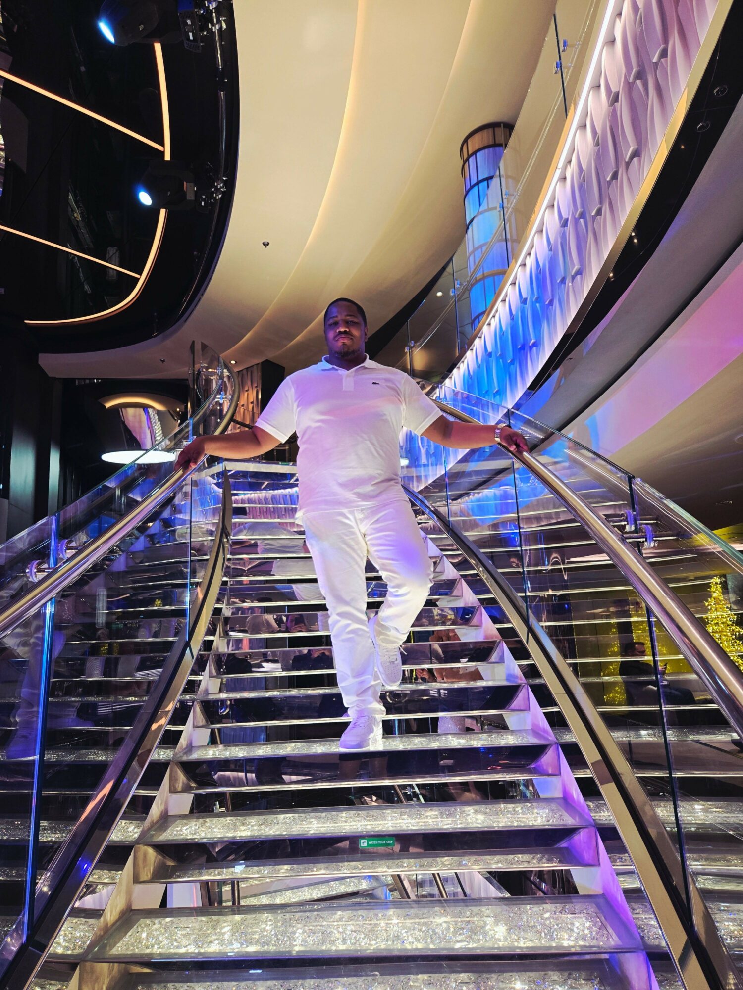 Person in white outfit leaning on a railing inside a modern, colorful building with curved architecture and illuminated displays.
