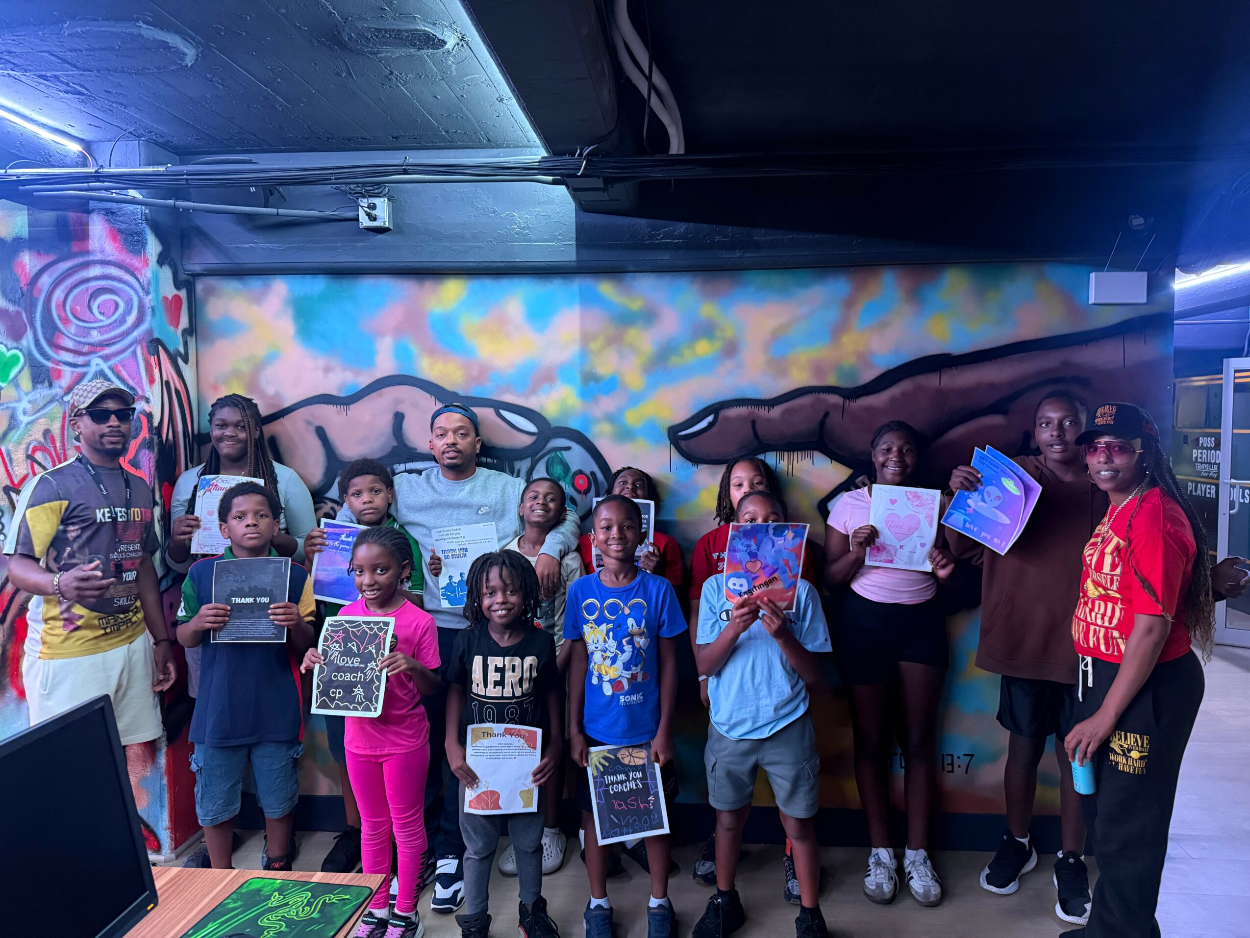 Group of children and adults standing in front of a colorful graffiti wall, holding books and papers, indoors.