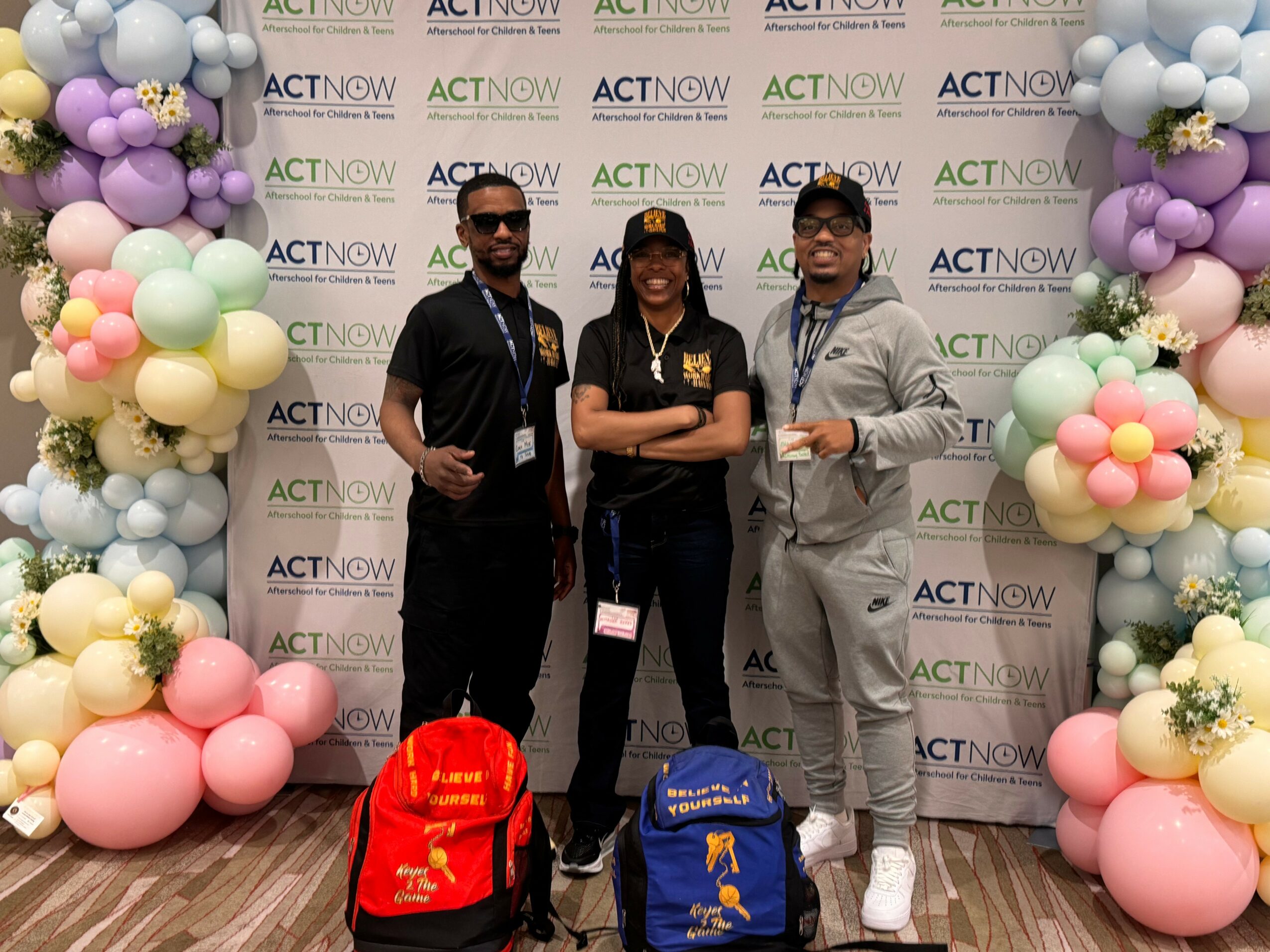 Three people stand in front of a backdrop with balloons on each side, smiling and posing for the photo.