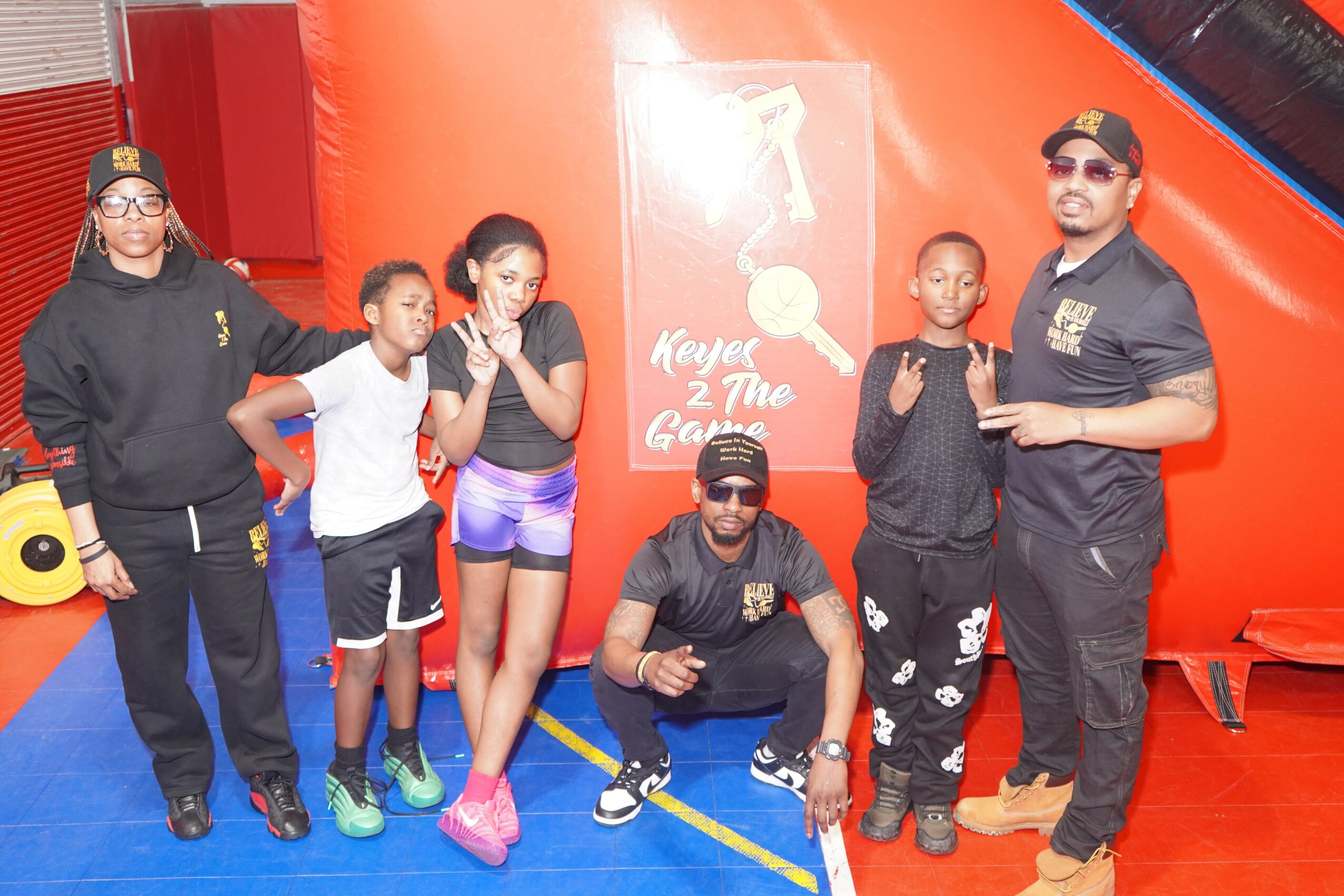 Group of six people, five children and one adult, standing in front of a red inflatable structure, smiling and posing for the photo.