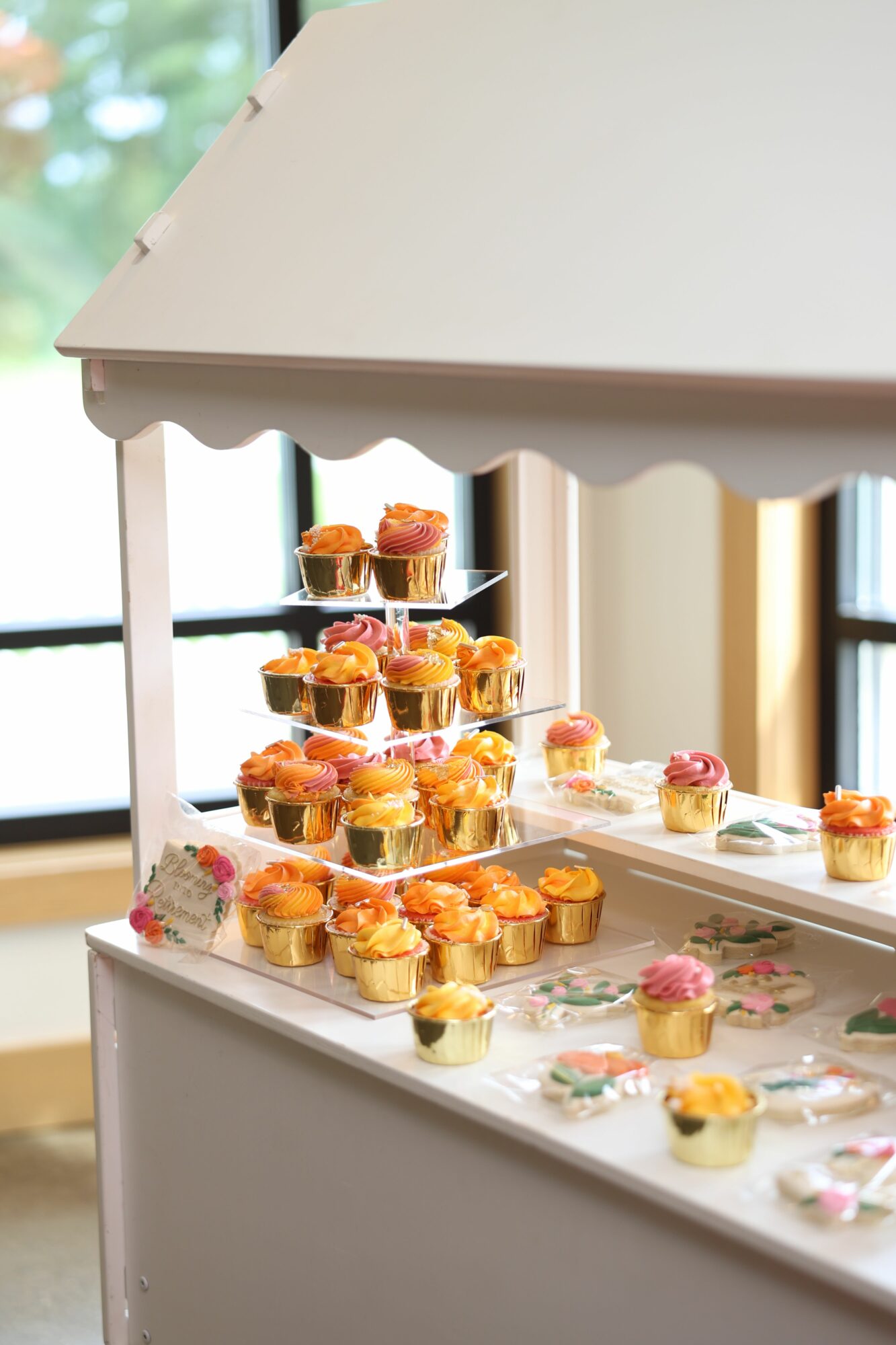 Multiple small desserts on a tiered stand, with a window in the background, viewed from the side.