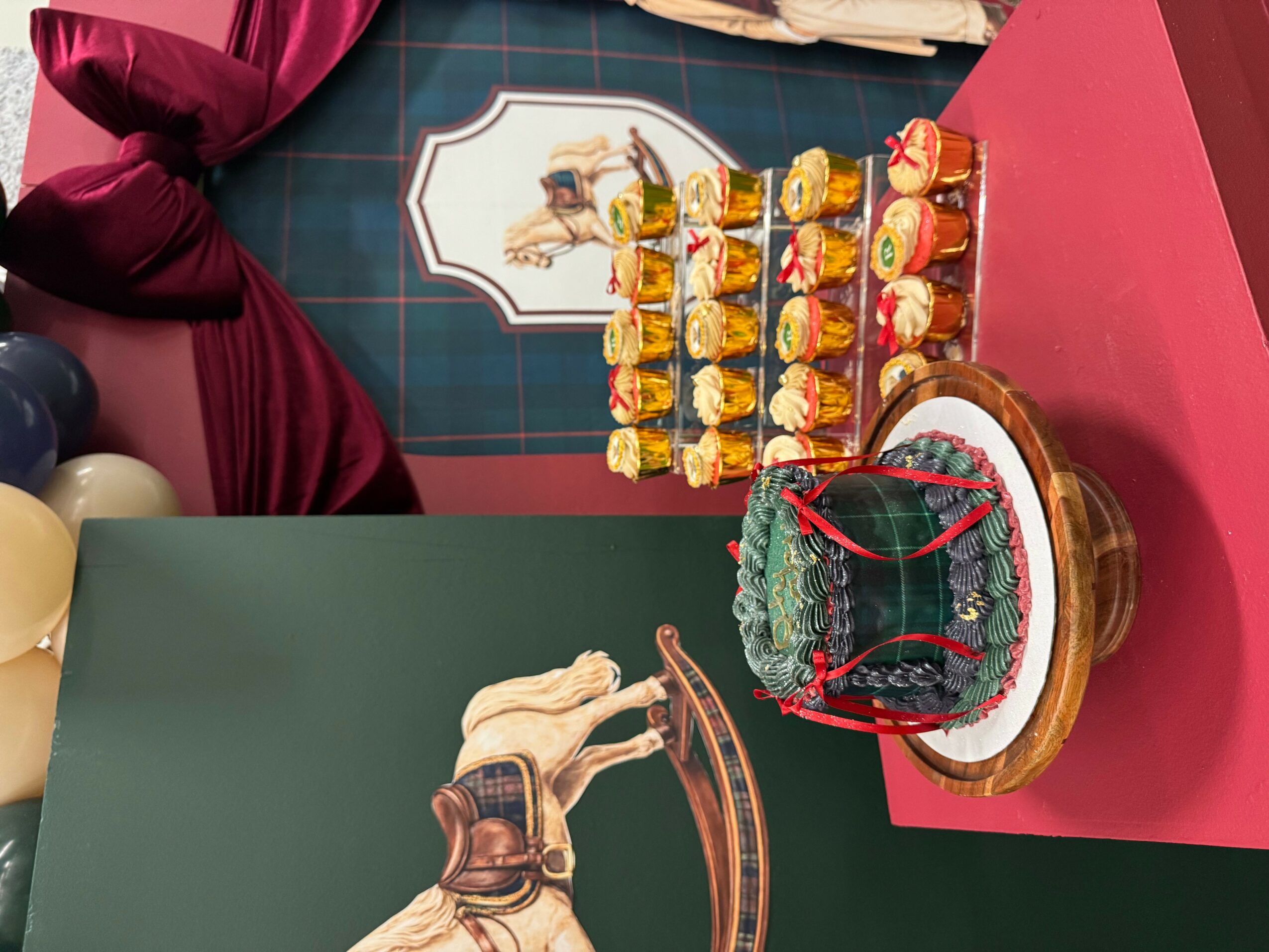 Display of colorful desserts on a tiered stand and a decorated cake on a table, with a person in a red shirt nearby.