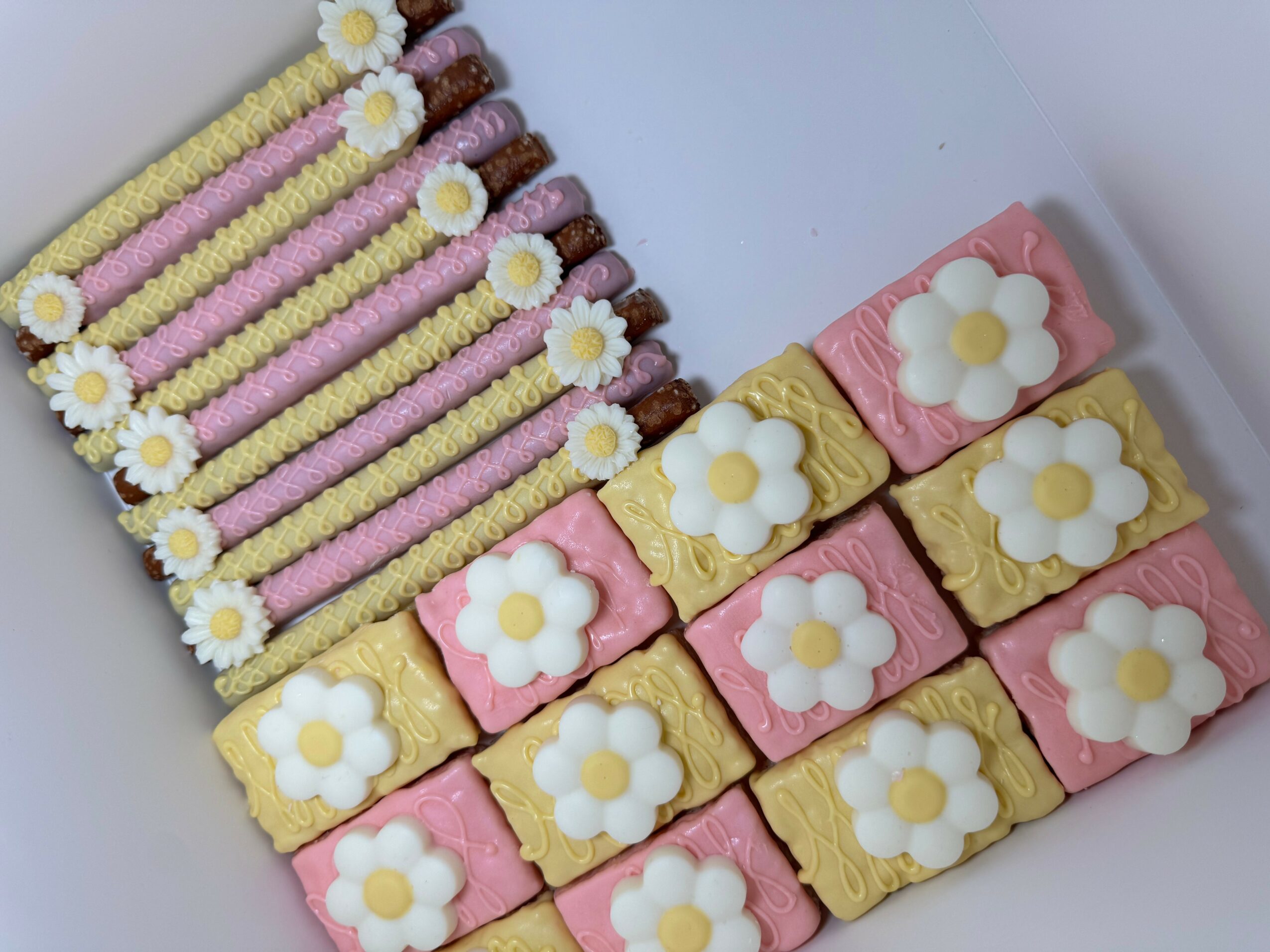 Decorative cookies with pink, yellow, and white icing, arranged in rows with floral designs.