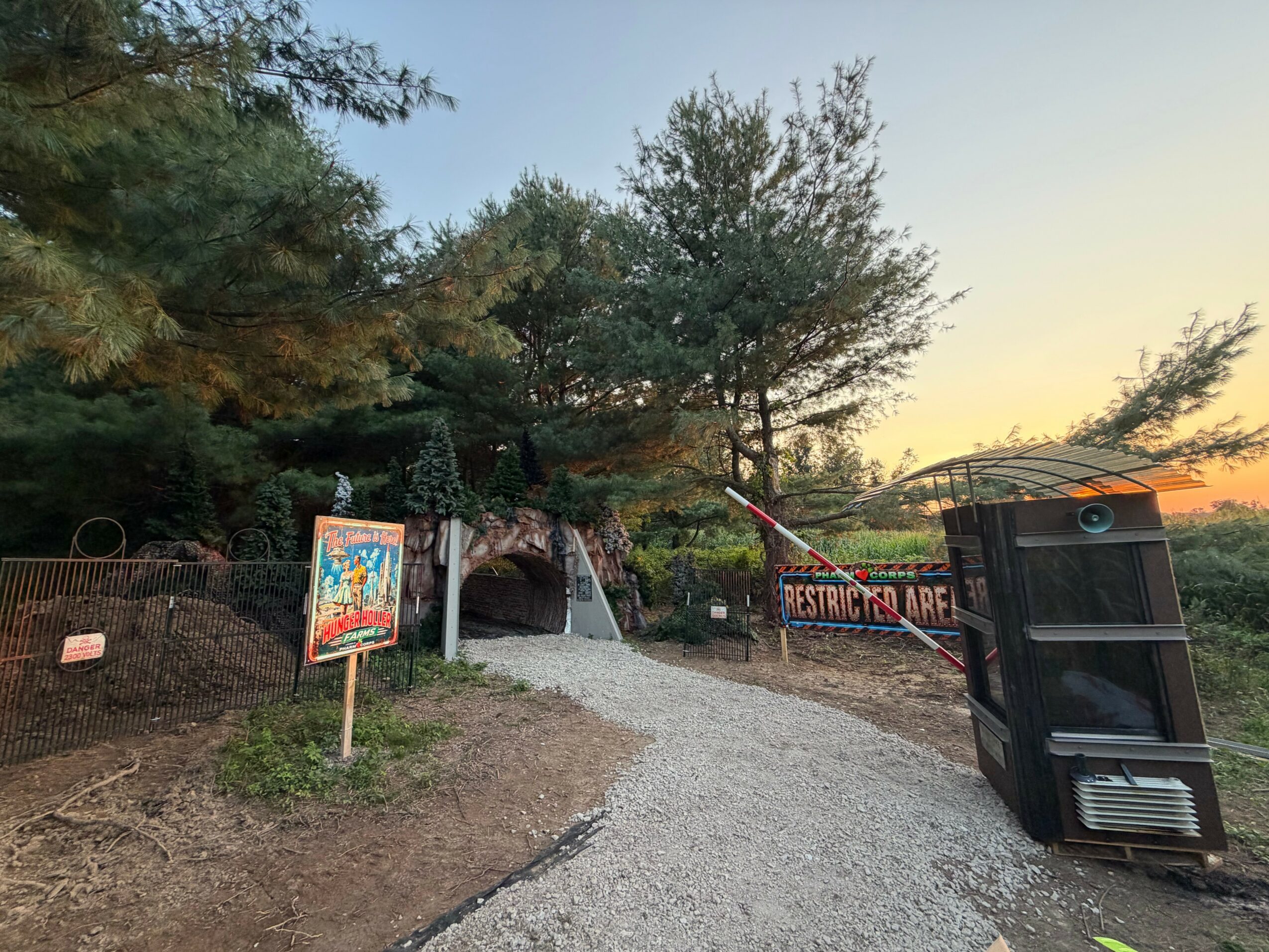 Path leading into a tunnel surrounded by trees, with a sign and a barrier on the side, under a clear sky.