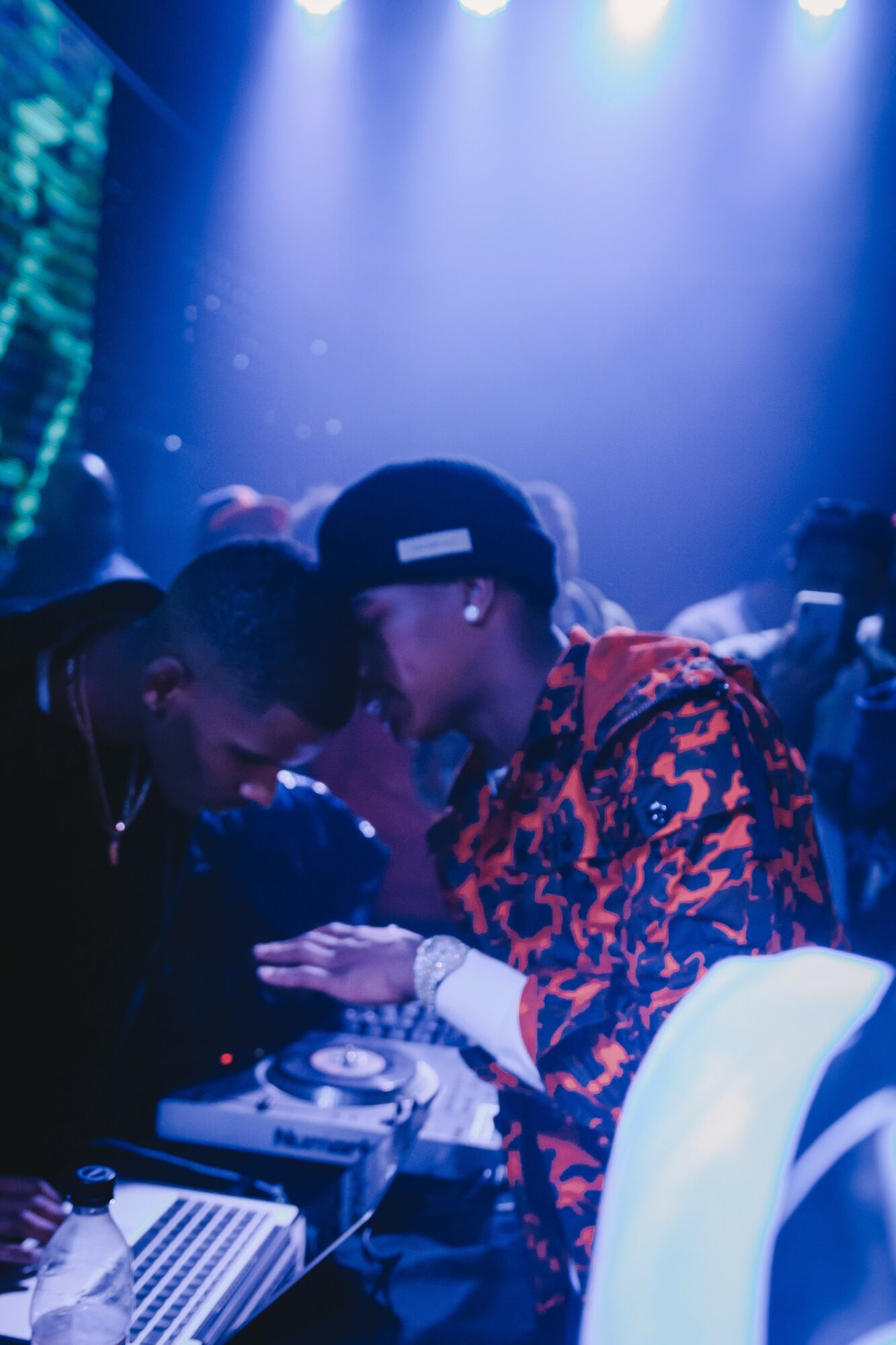 Two people are closely interacting at a nightclub with blue and purple lighting, surrounded by a crowd.