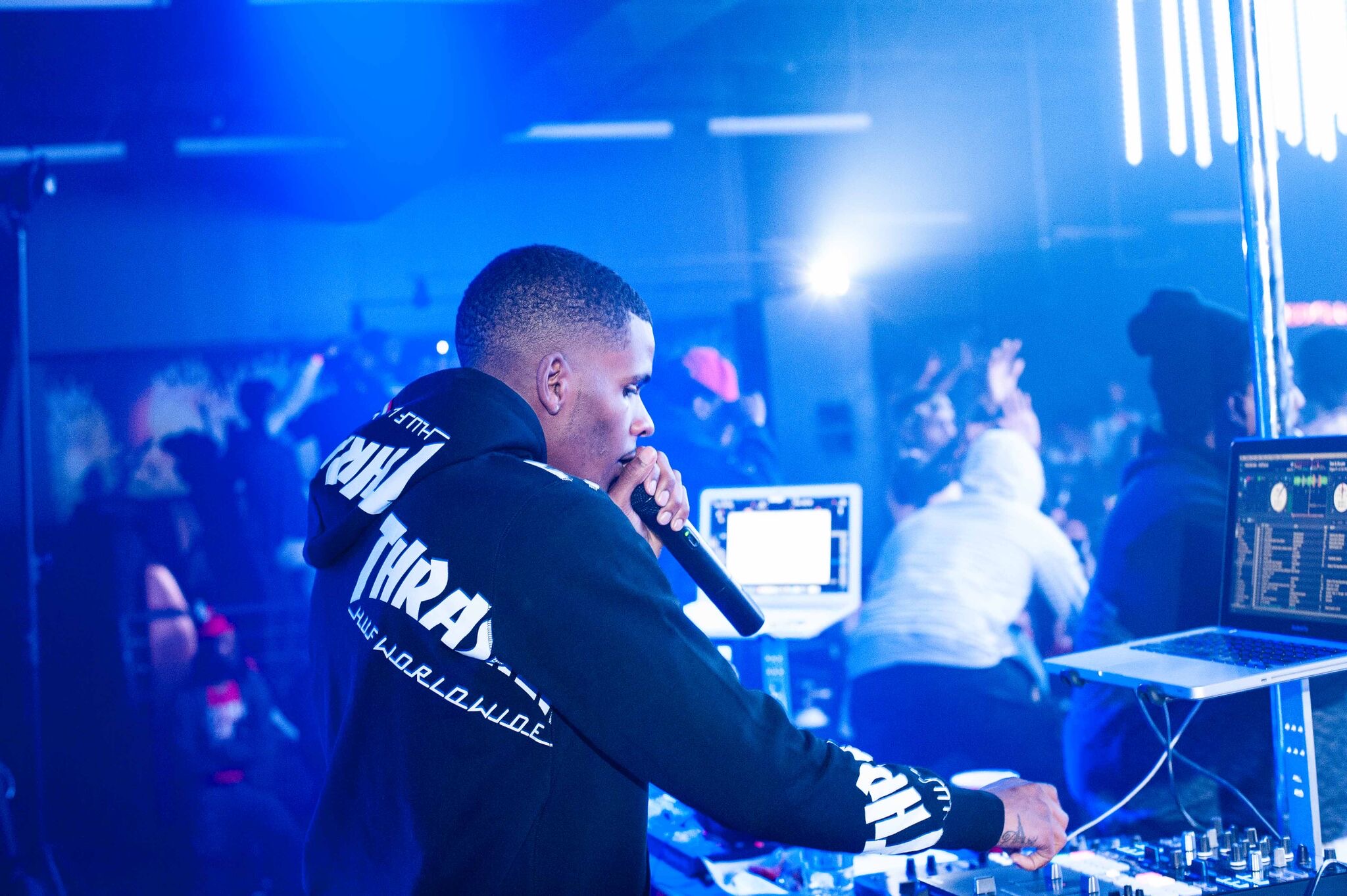 DJ performing at a nightclub with blue lighting and a crowd in the background.