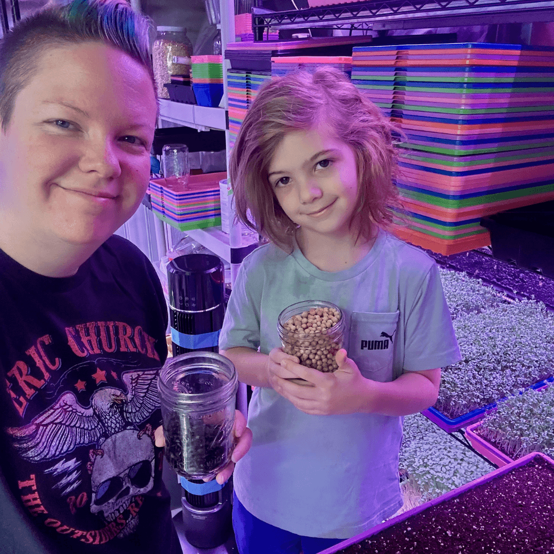 Two children, a boy and a girl, standing in front of colorful stacked objects, holding a jar of beans, smiling.