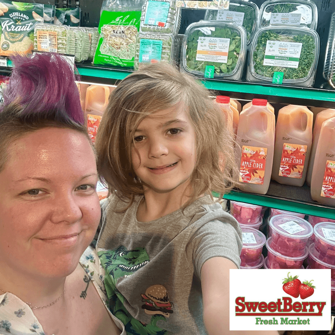 A woman and a young girl taking a selfie in a grocery store aisle with packaged food items behind them.