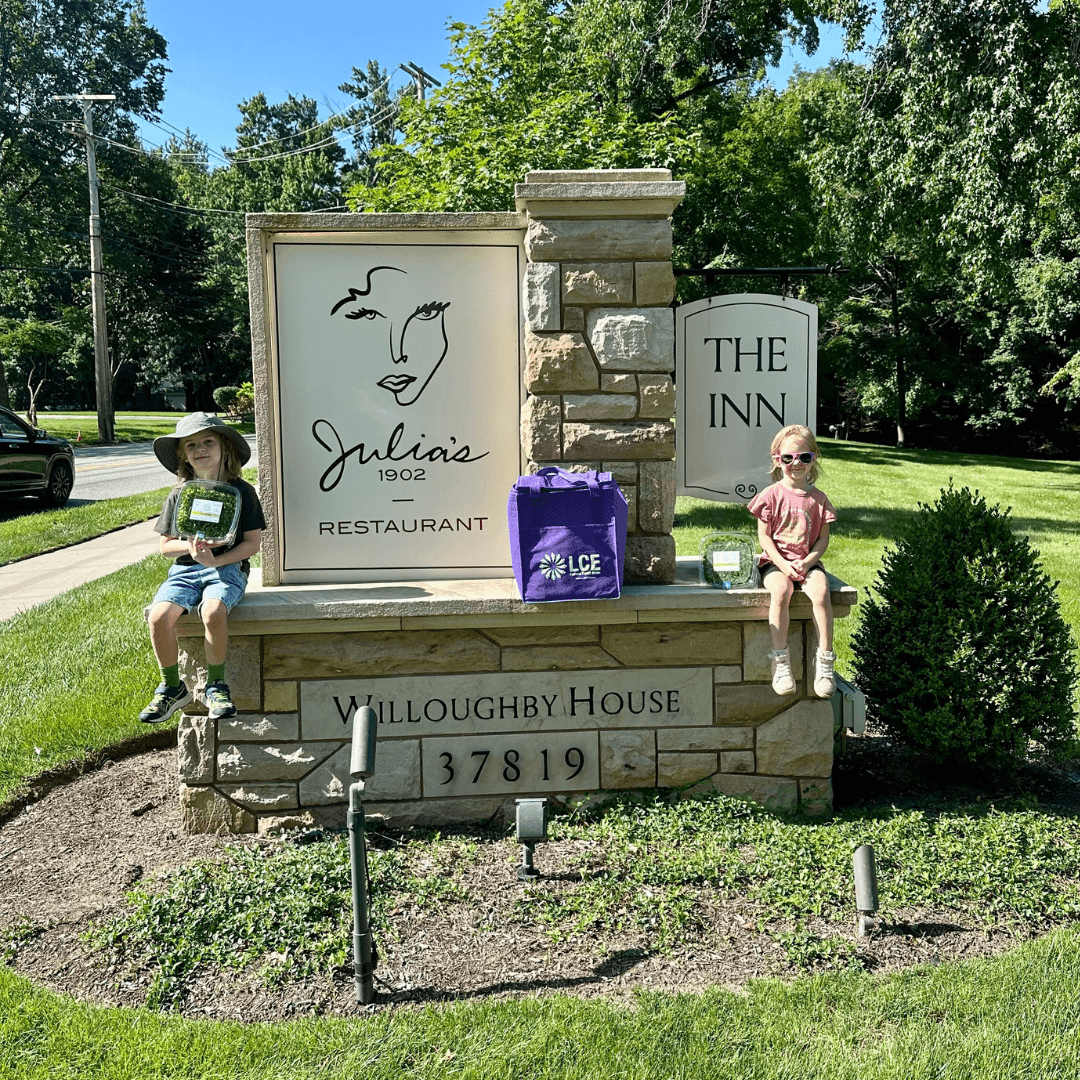 Two children sitting on stone ledge in front of a sign for Julie's restaurant and The Inn, with trees and grass behind.