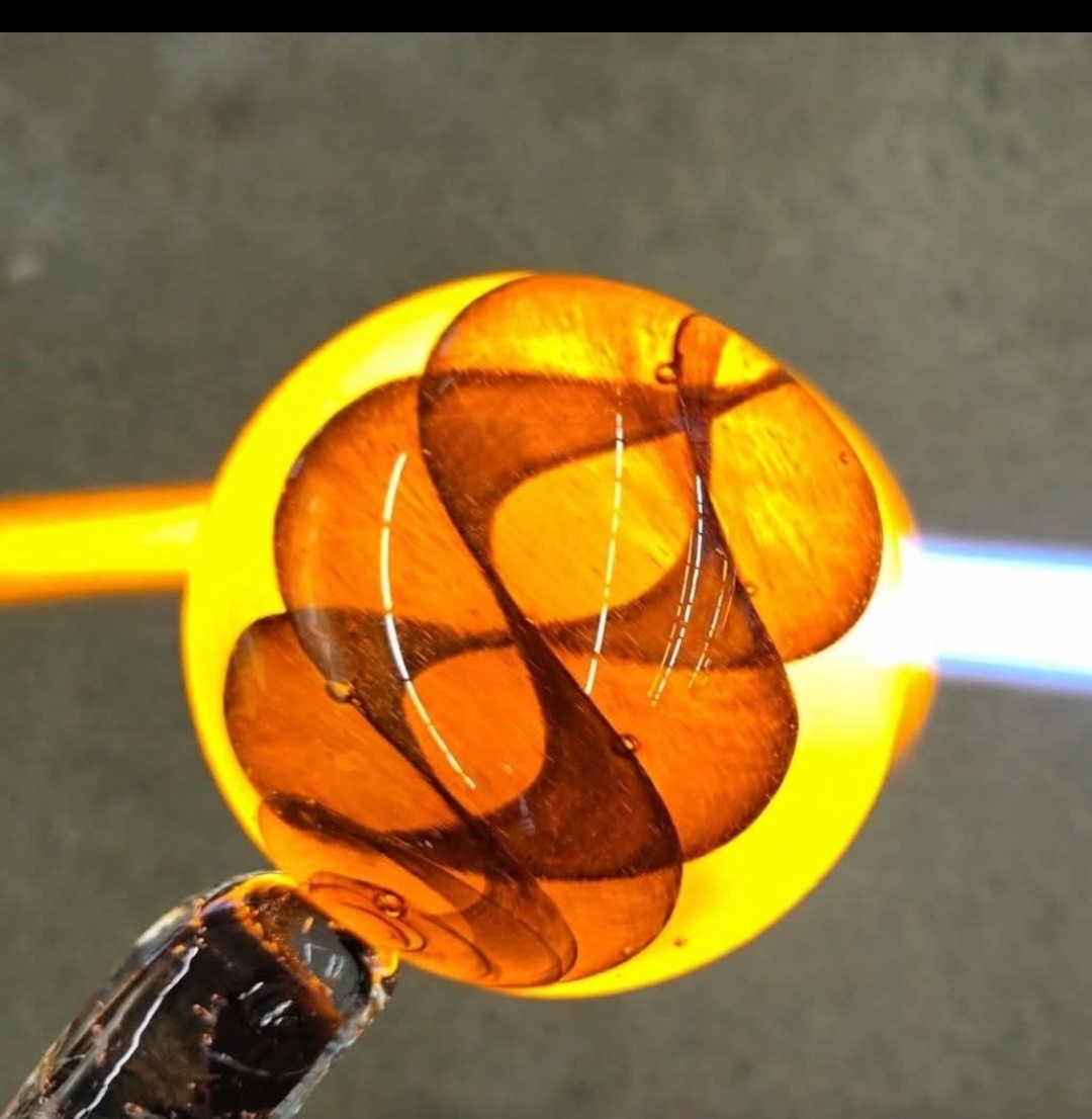 Close-up of a glass object with orange and yellow hues, with a yellow handle and a gray background.
