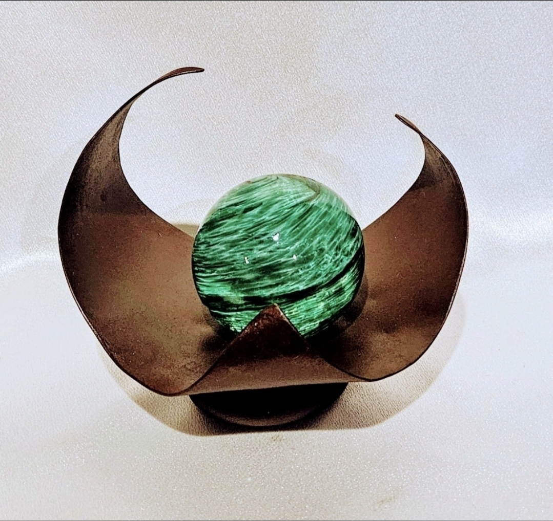 A decorative object with a green marbled sphere inside a curved, metallic structure resembling a crescent moon, on a white background.