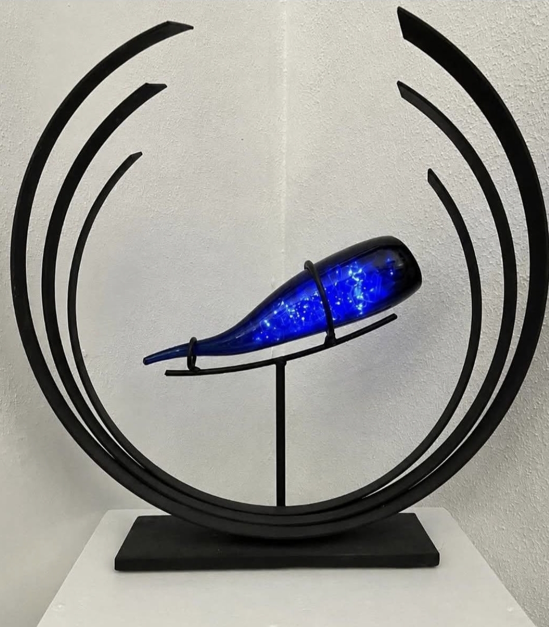 Decorative sculpture with a blue, galaxy-like object inside a black circular frame, mounted on a stand. Word count: 20.
