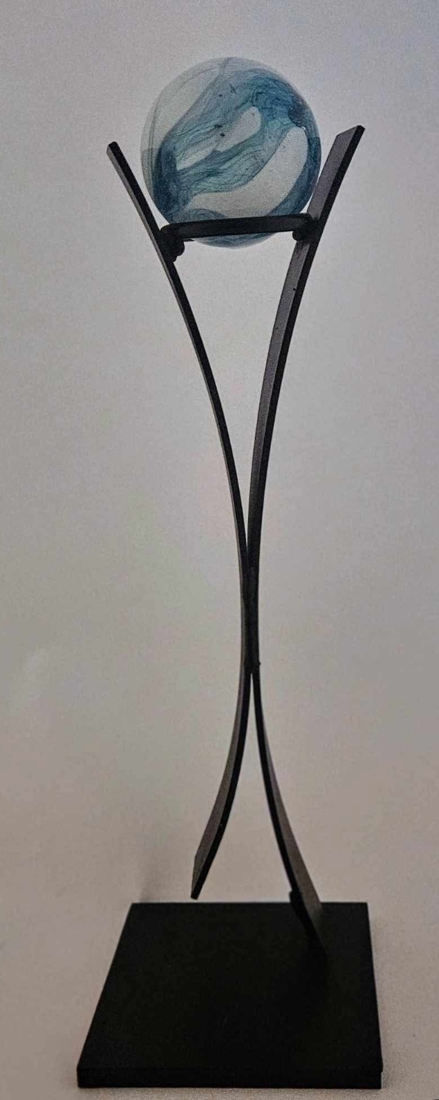 Decorative sculpture with a glass sphere on a black stand, set against a plain background.