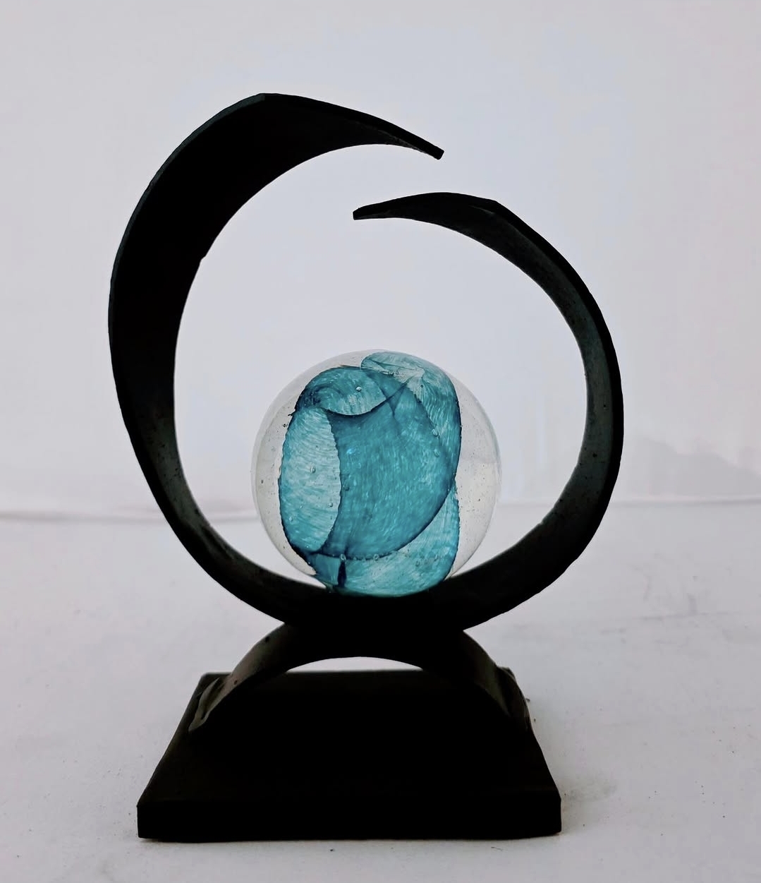 Sculpture with a black circular frame and a blue glass element inside, mounted on a black base.