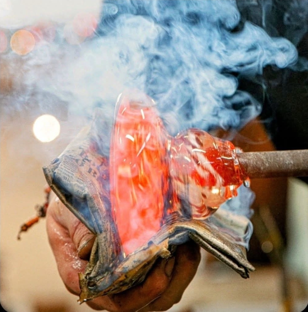 Person holding a burning, glowing object with smoke rising, in a close-up shot.