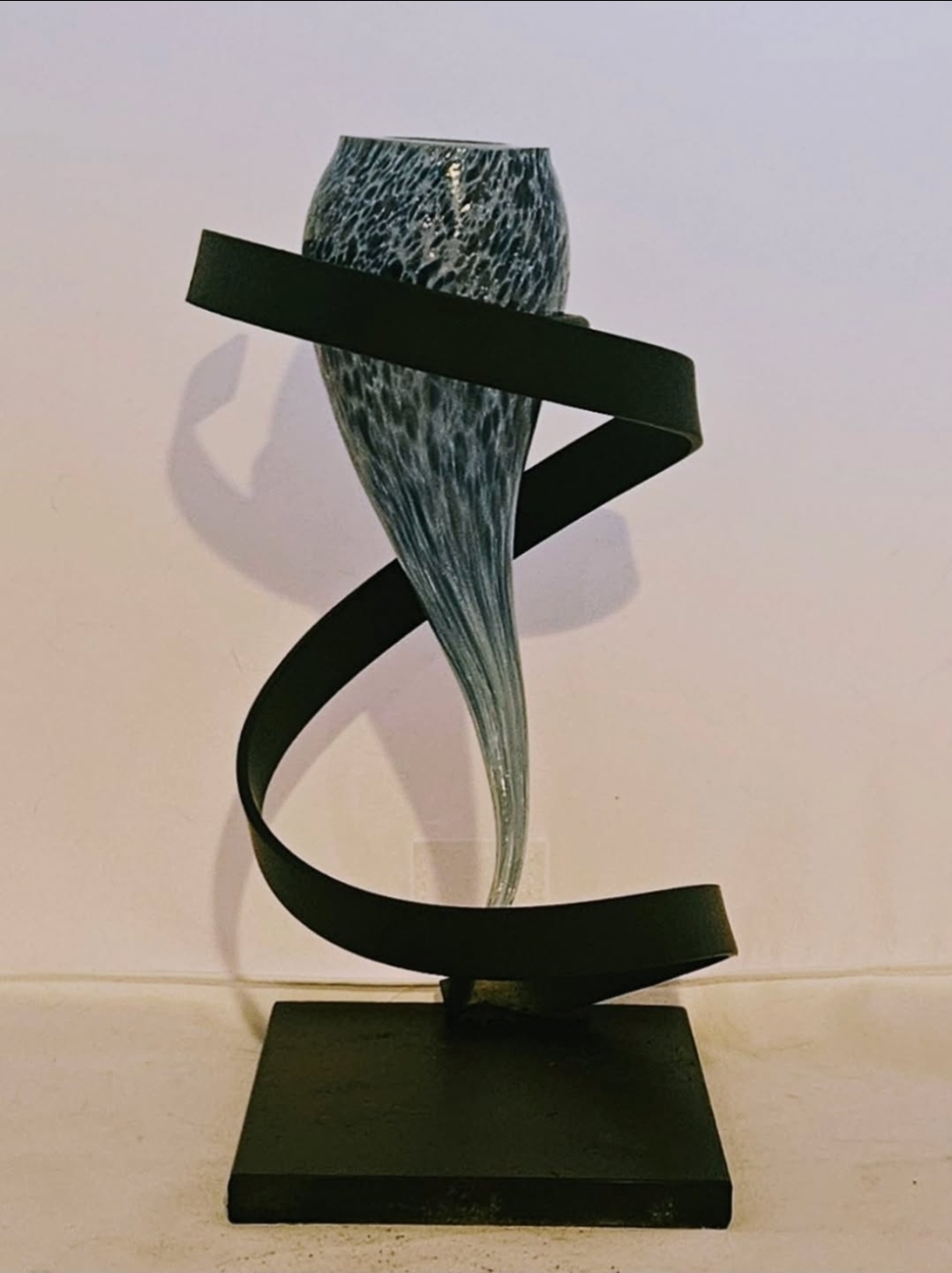 Sculpture with a textured top, twisting black ribbon, and a flowing base on a black square platform.