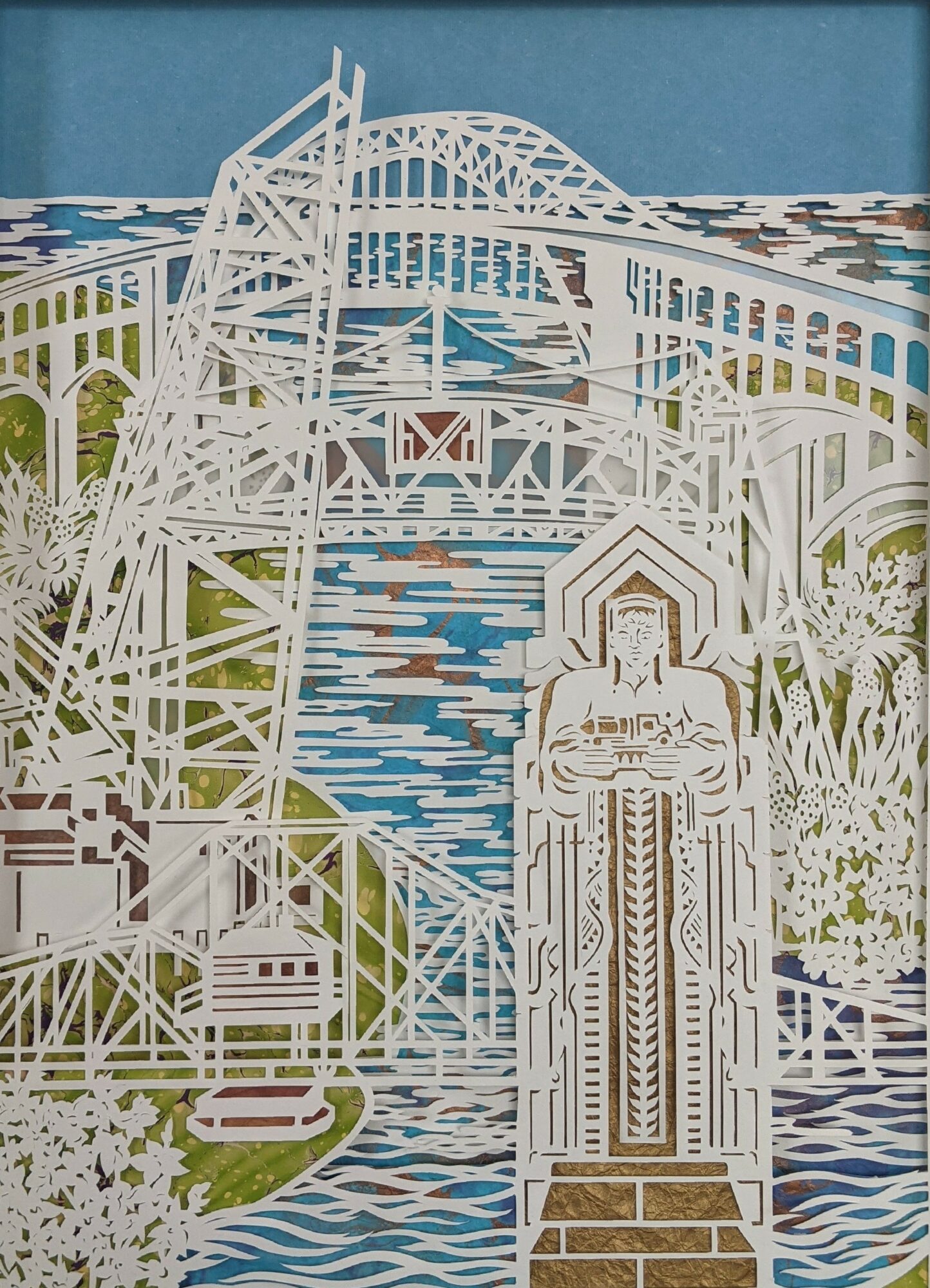 White paper cutout of a roller coaster, bridge, and statue with trees and water in background.