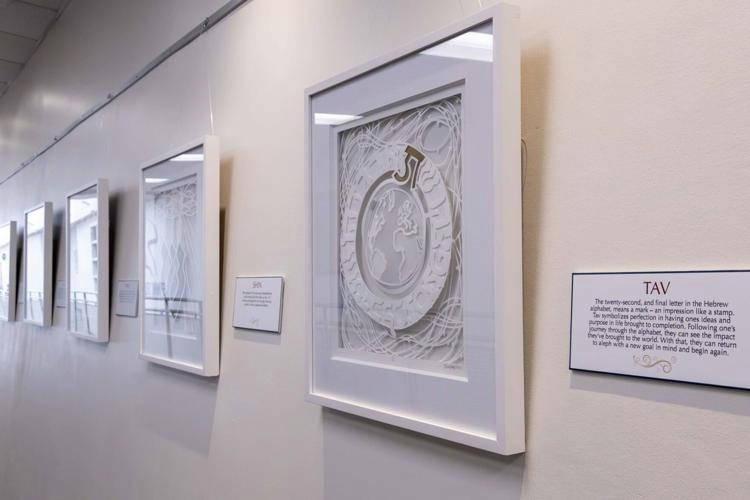 Gallery wall with framed artwork and informational plaques, viewed from the right side, with white walls and ceiling.