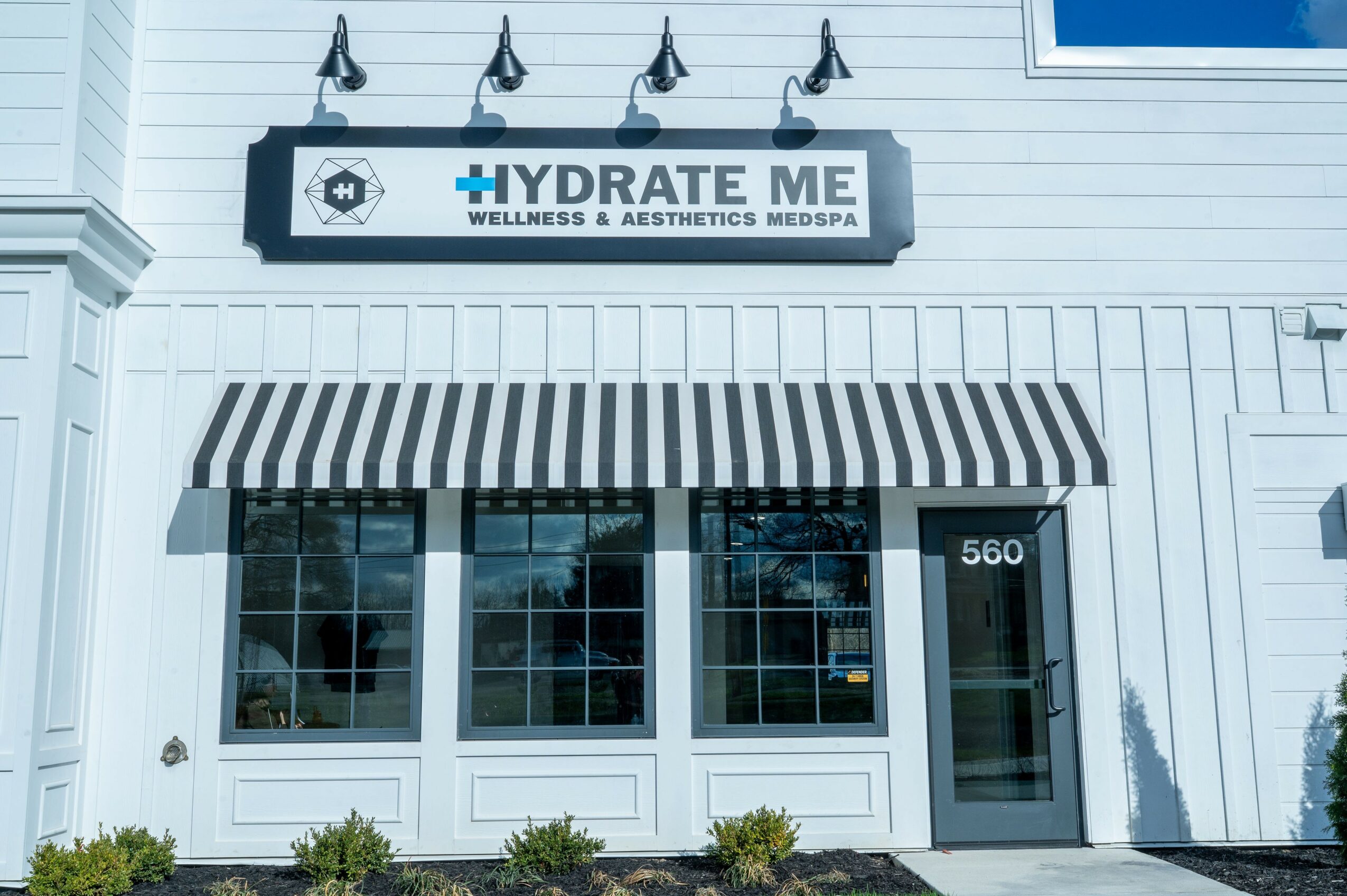 Storefront with striped awning, large windows, and a door numbered 560, with a sign reading 'HYDRATE ME' above.