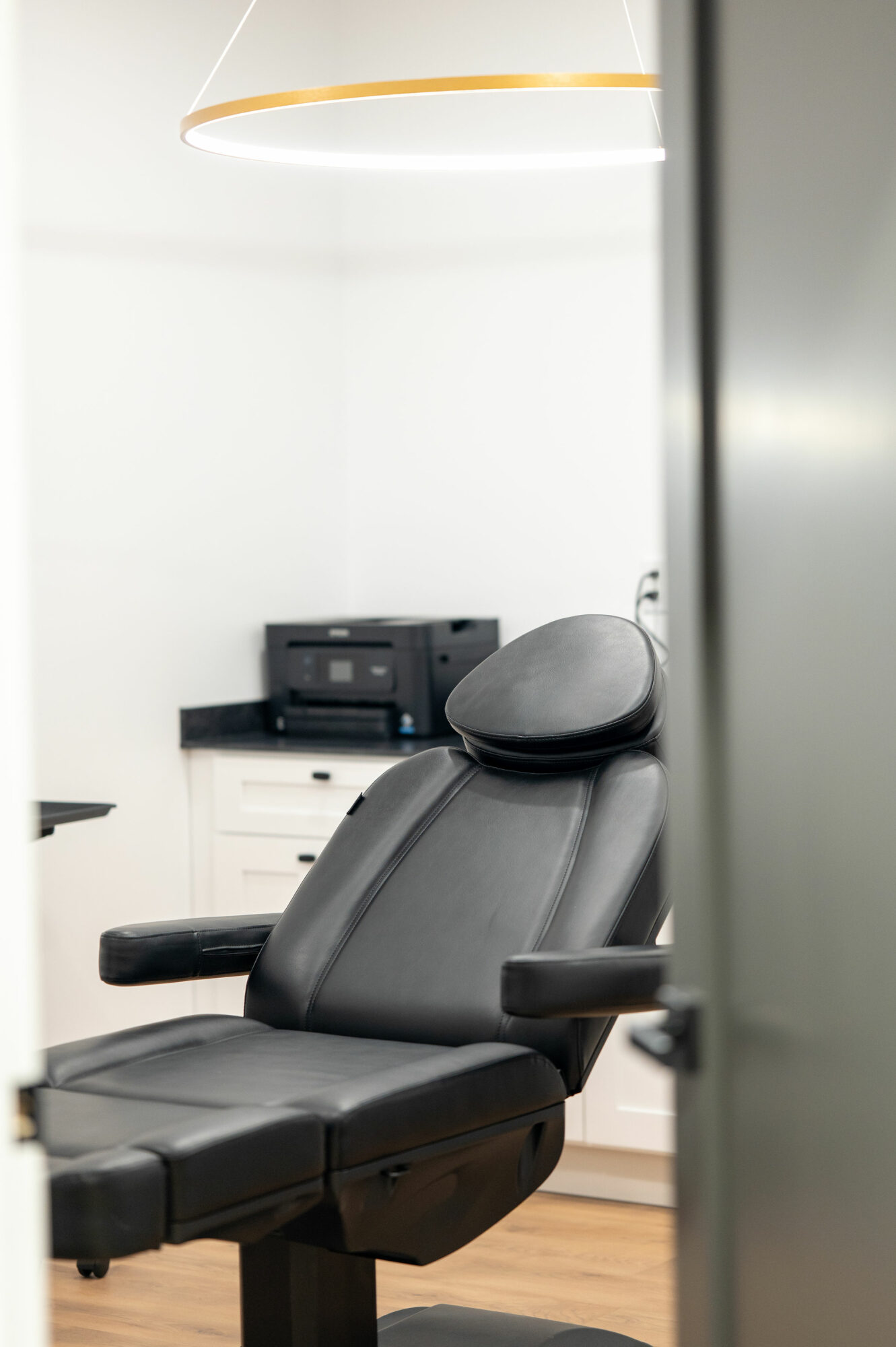 Office chair in a room with a printer and white cabinets, viewed partially through a door frame.