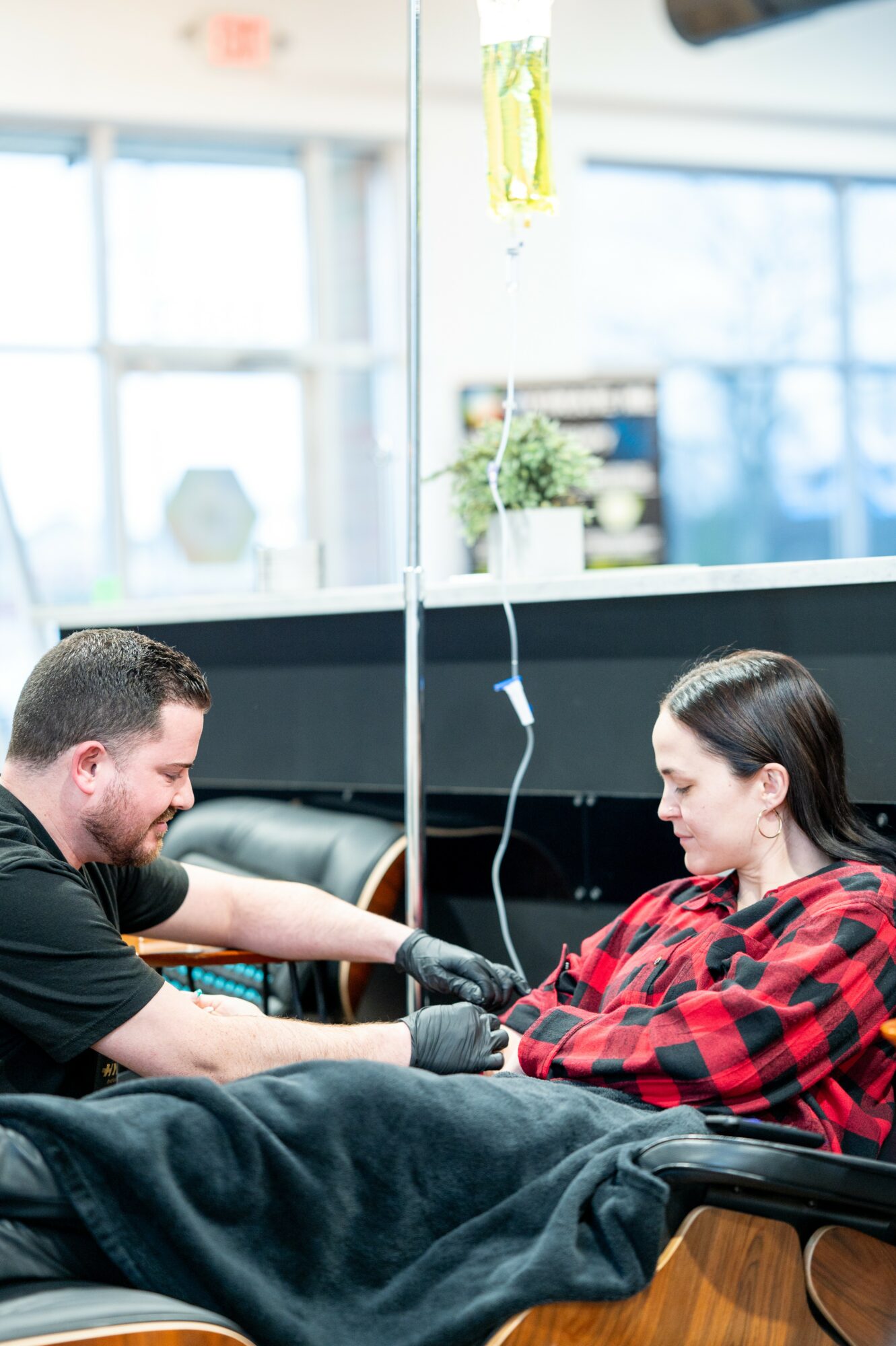 A person receiving medical treatment from a healthcare worker in a clinical setting, with IV drip and medical equipment visible.