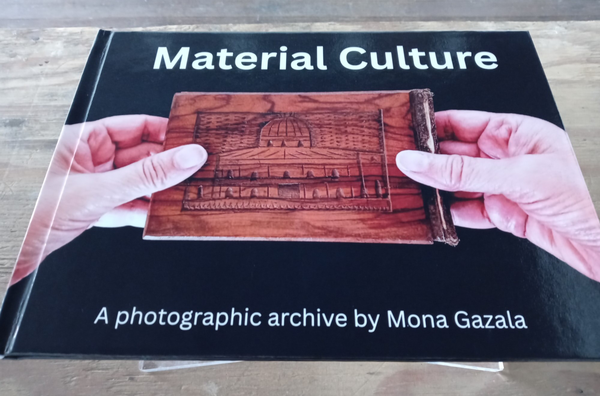 Book titled 'Material Culture' with hands holding a wooden object, on a gray surface.
