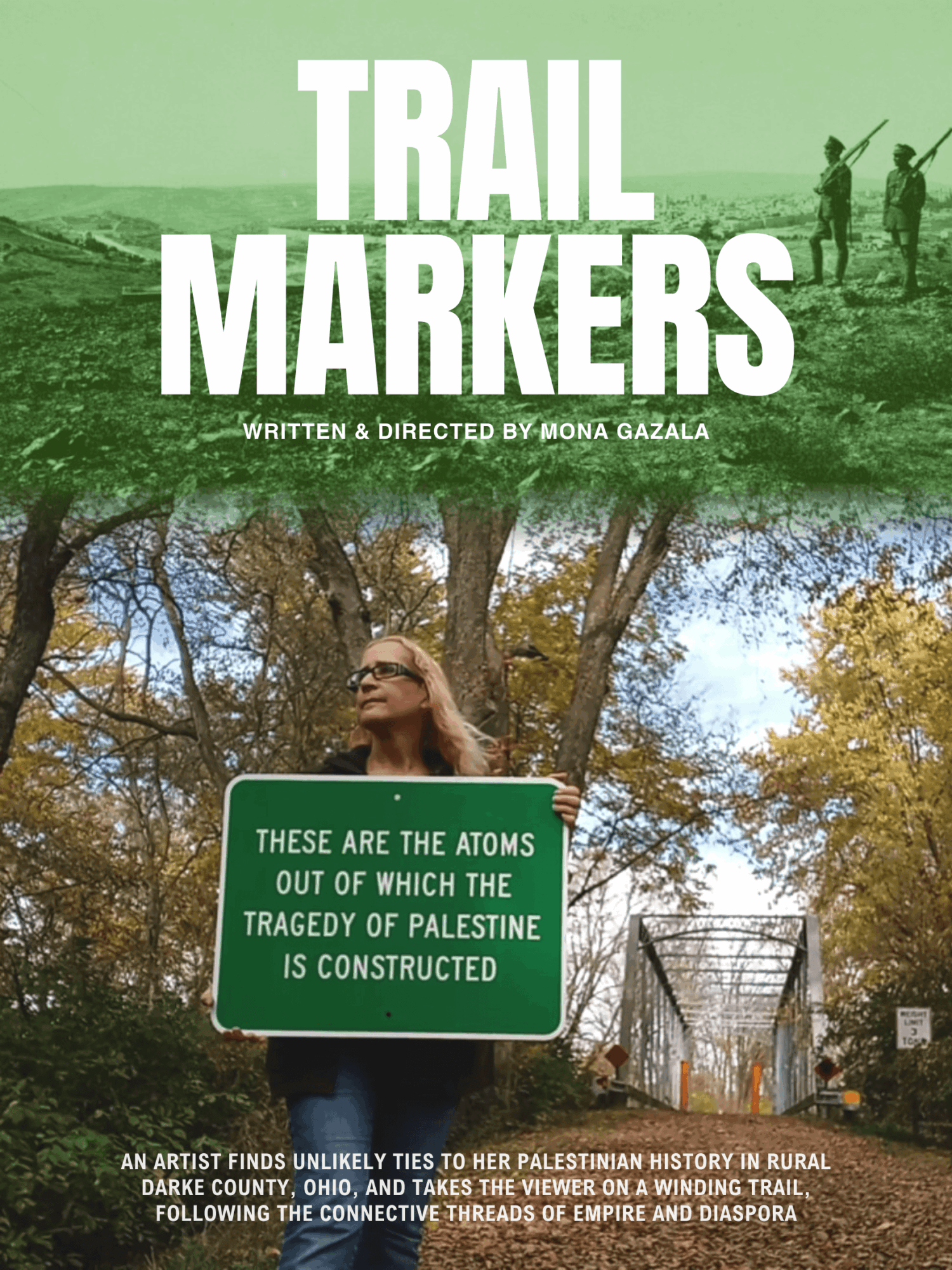 Group of people walking on a trail with trees and a woman holding a sign in a park.