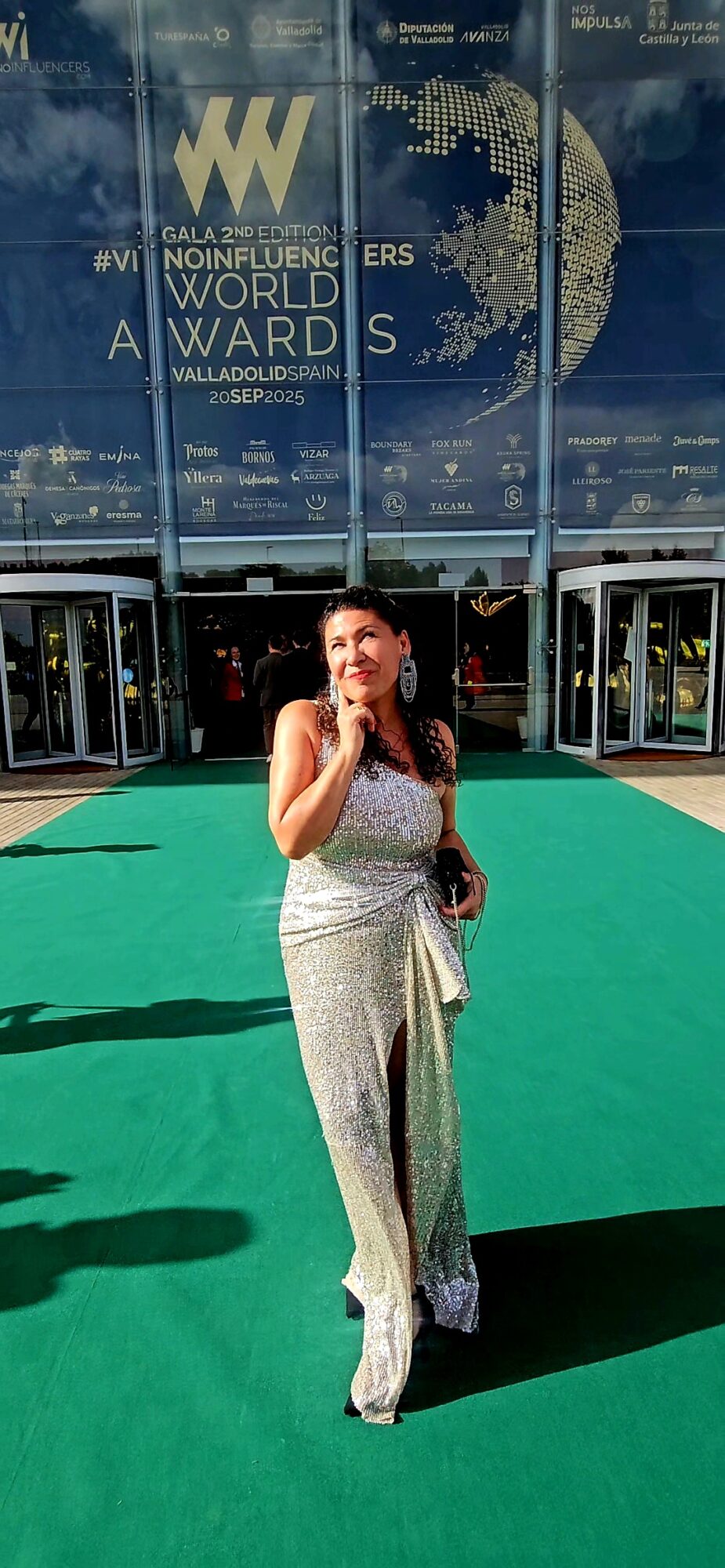 Woman in patterned dress standing on green carpet outside conference center, with glass building and World Word logo in background.