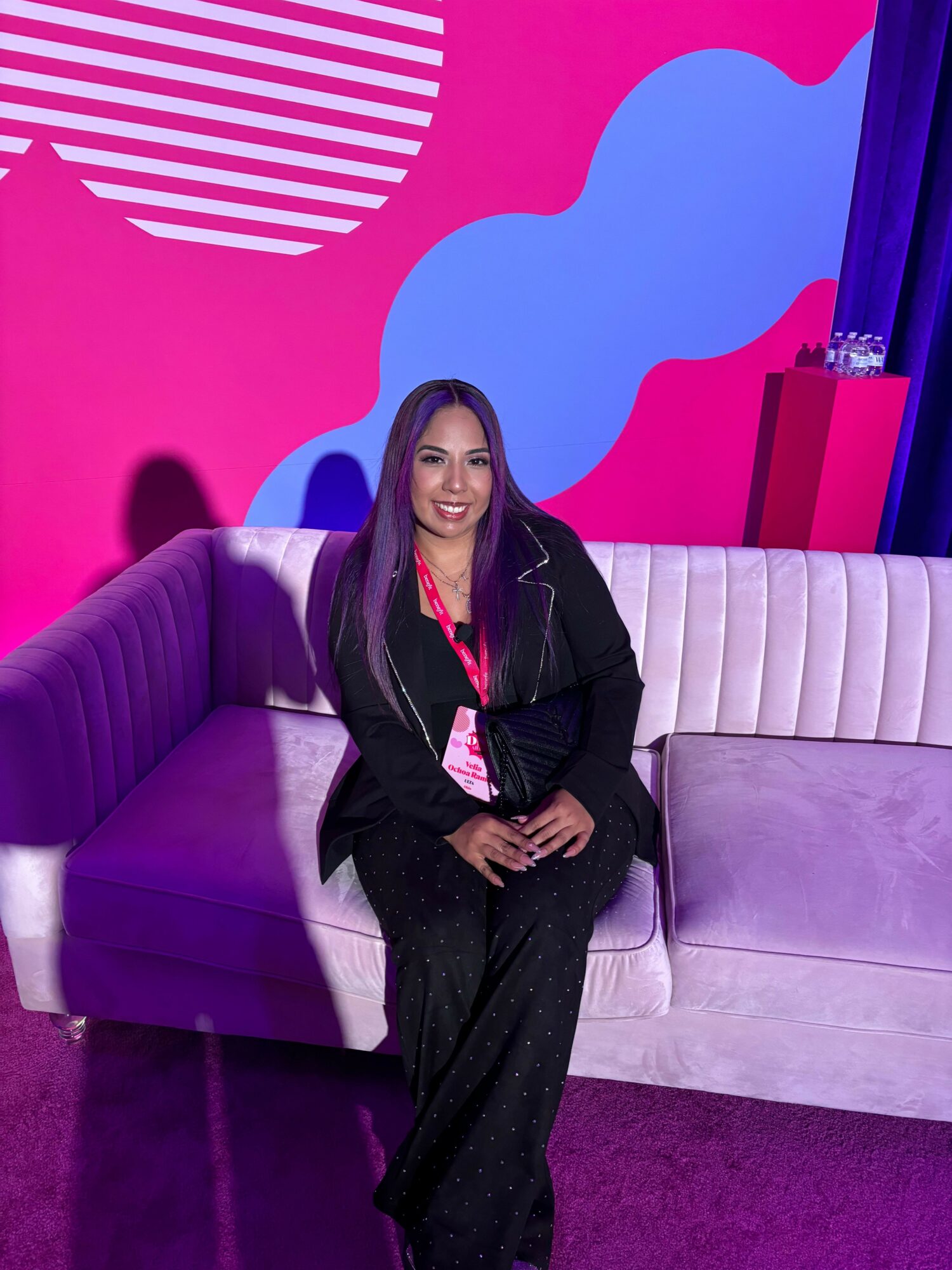Woman sitting on a purple sofa in a colorful studio with pink, blue, and purple background elements.