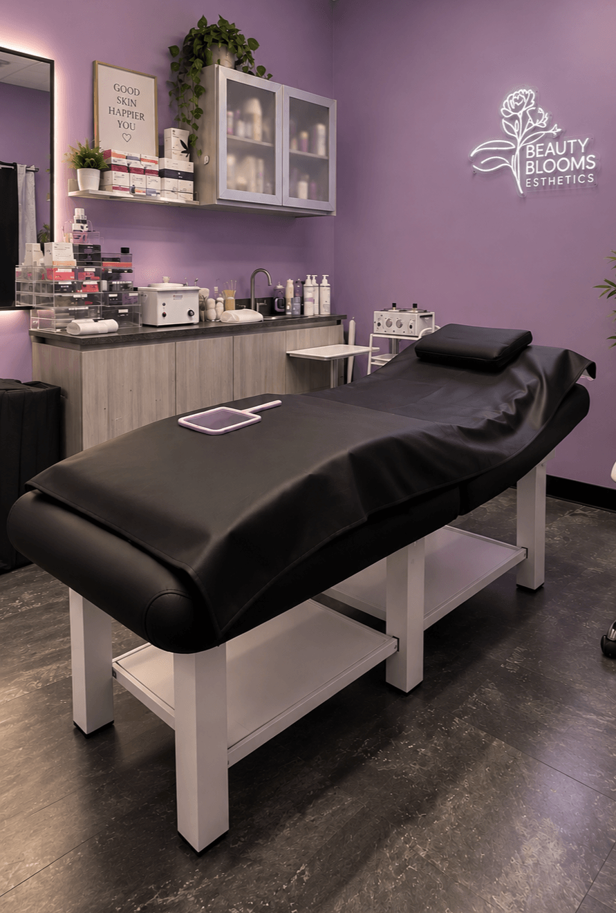 Treatment bed covered with black sheet in a room with purple walls, shelves, and beauty products, logo on wall.