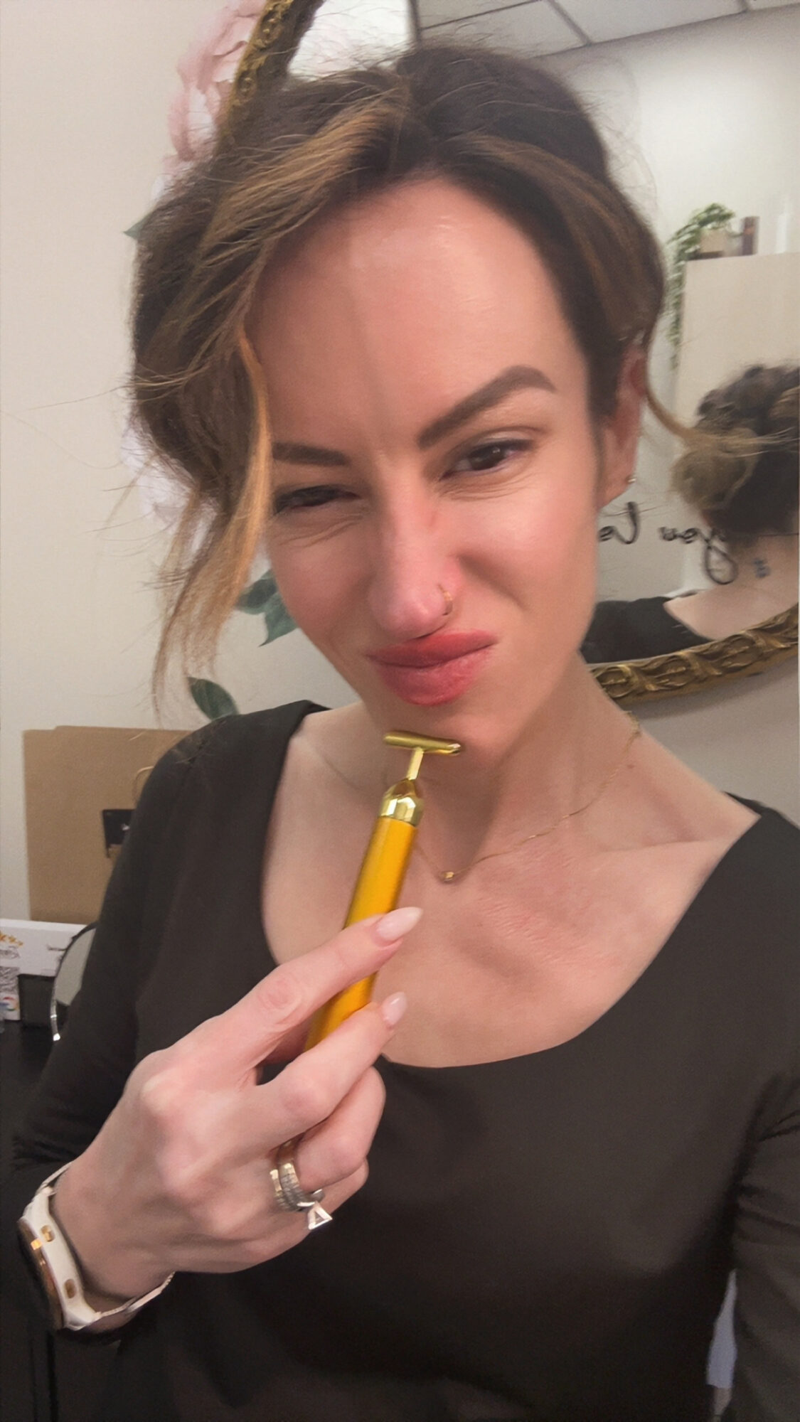 Woman with dark hair and makeup holding a yellow object near her face, making a grimace, in an indoor setting.
