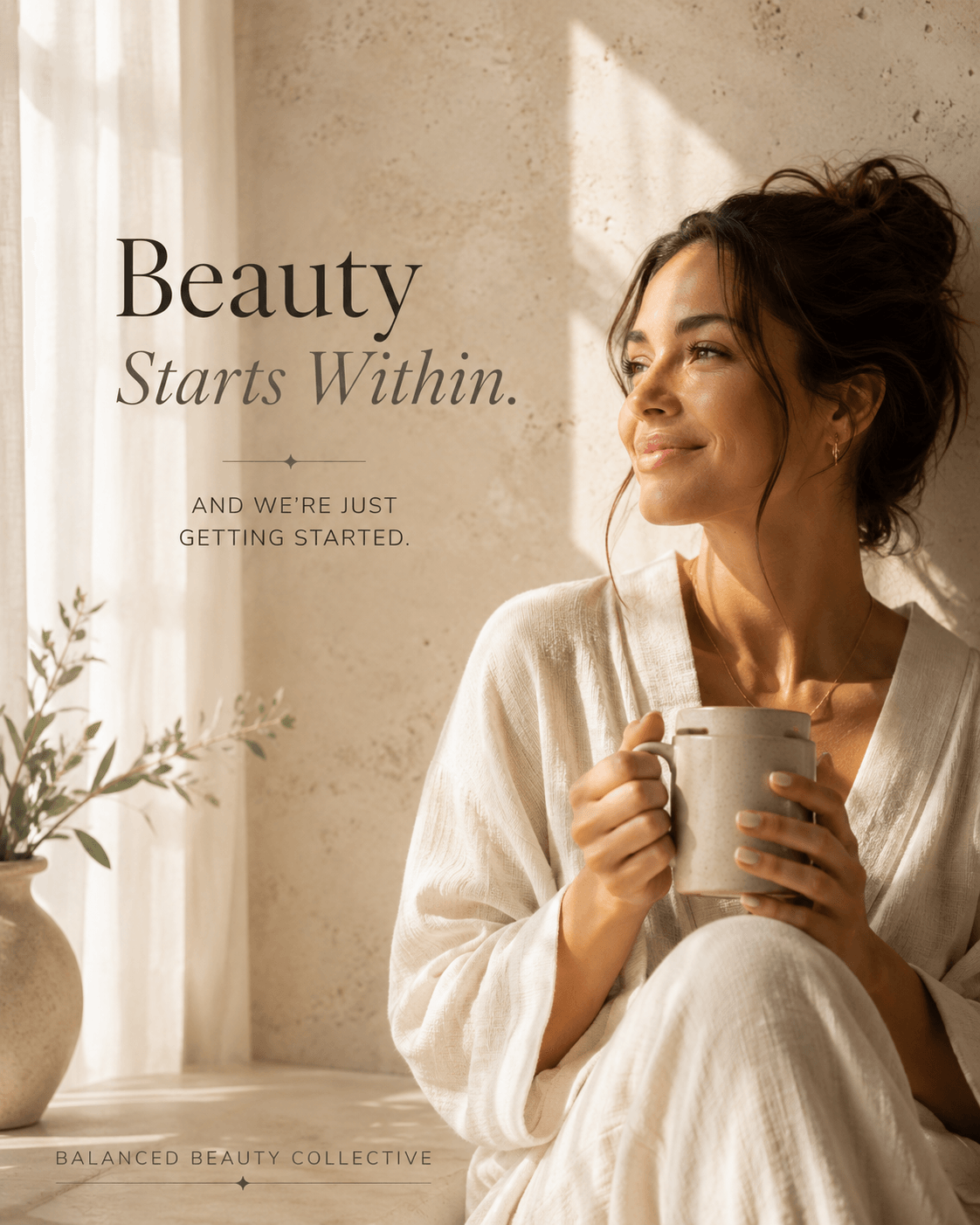 Woman with dark hair in a bun holding a mug, sitting near a window with sunlight, smiling, wearing a light-colored robe.