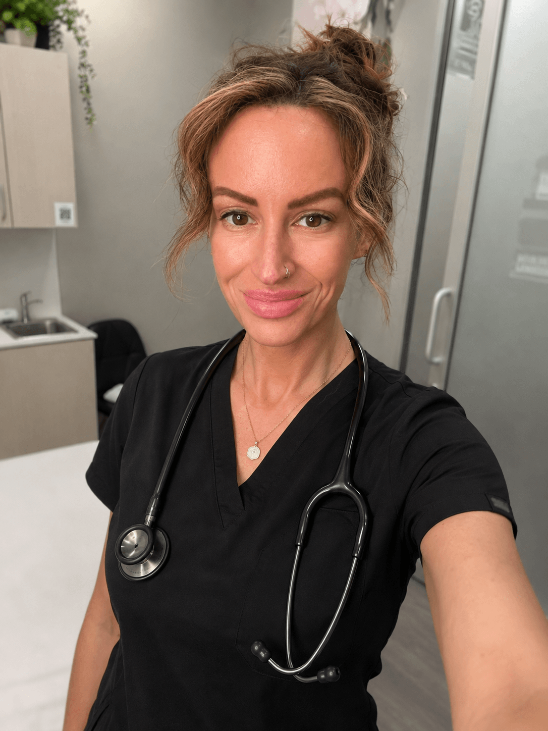 Female healthcare professional with a stethoscope around her neck, smiling, in a clinical setting.