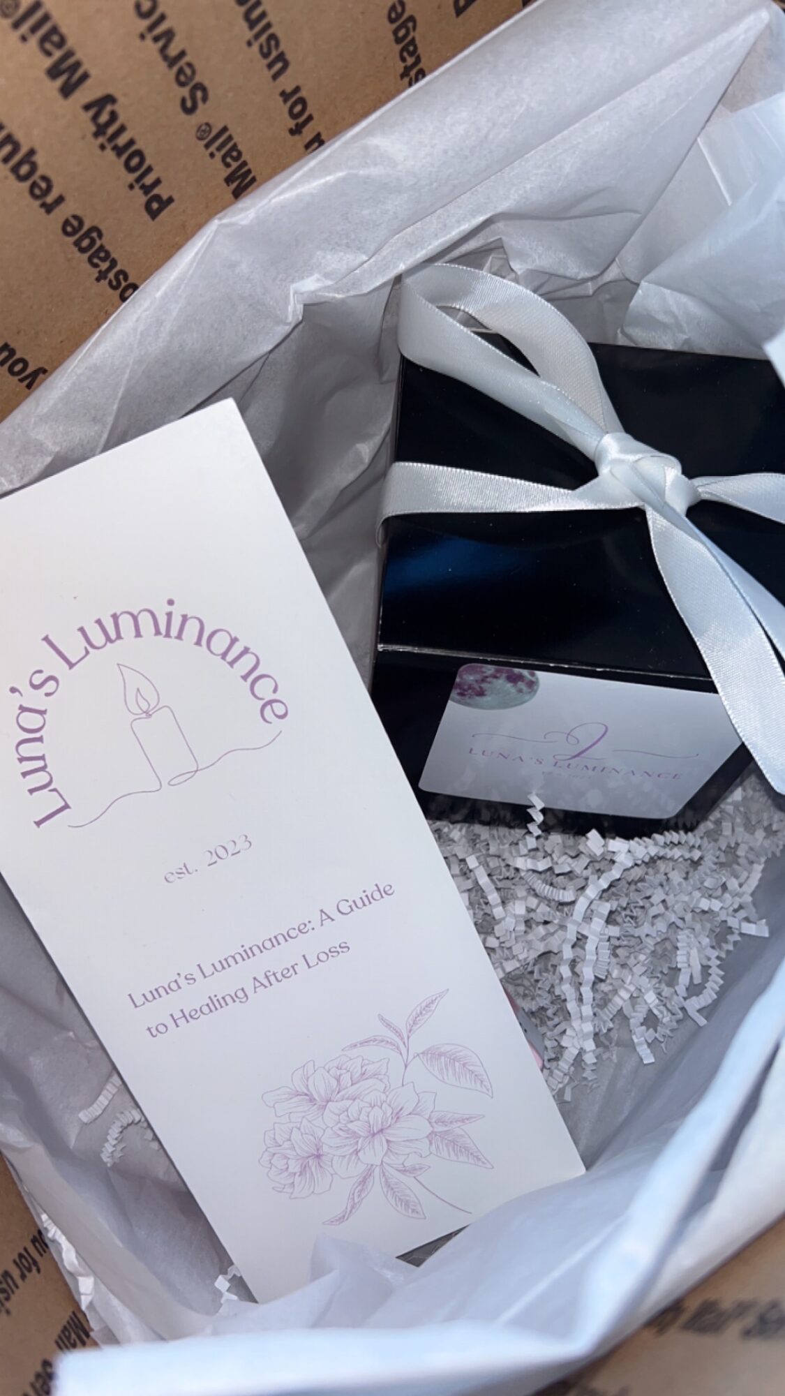 Gift box with a white ribbon, tissue paper, and a card inside a shopping bag.