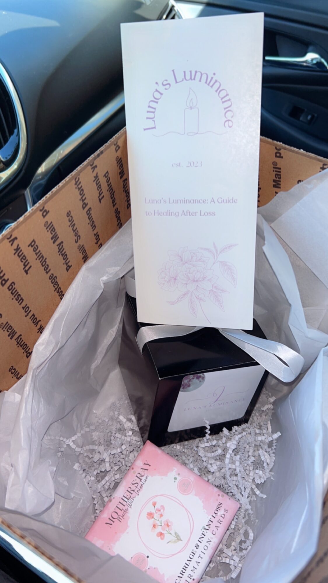 A white box with a tall, white card inside, surrounded by tissue paper and packaging materials in a box.