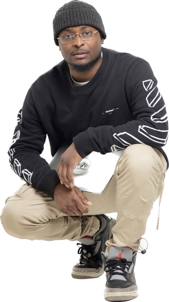 Person crouching, wearing a black beanie, glasses, black sweatshirt, beige pants, and sneakers, against a black background.