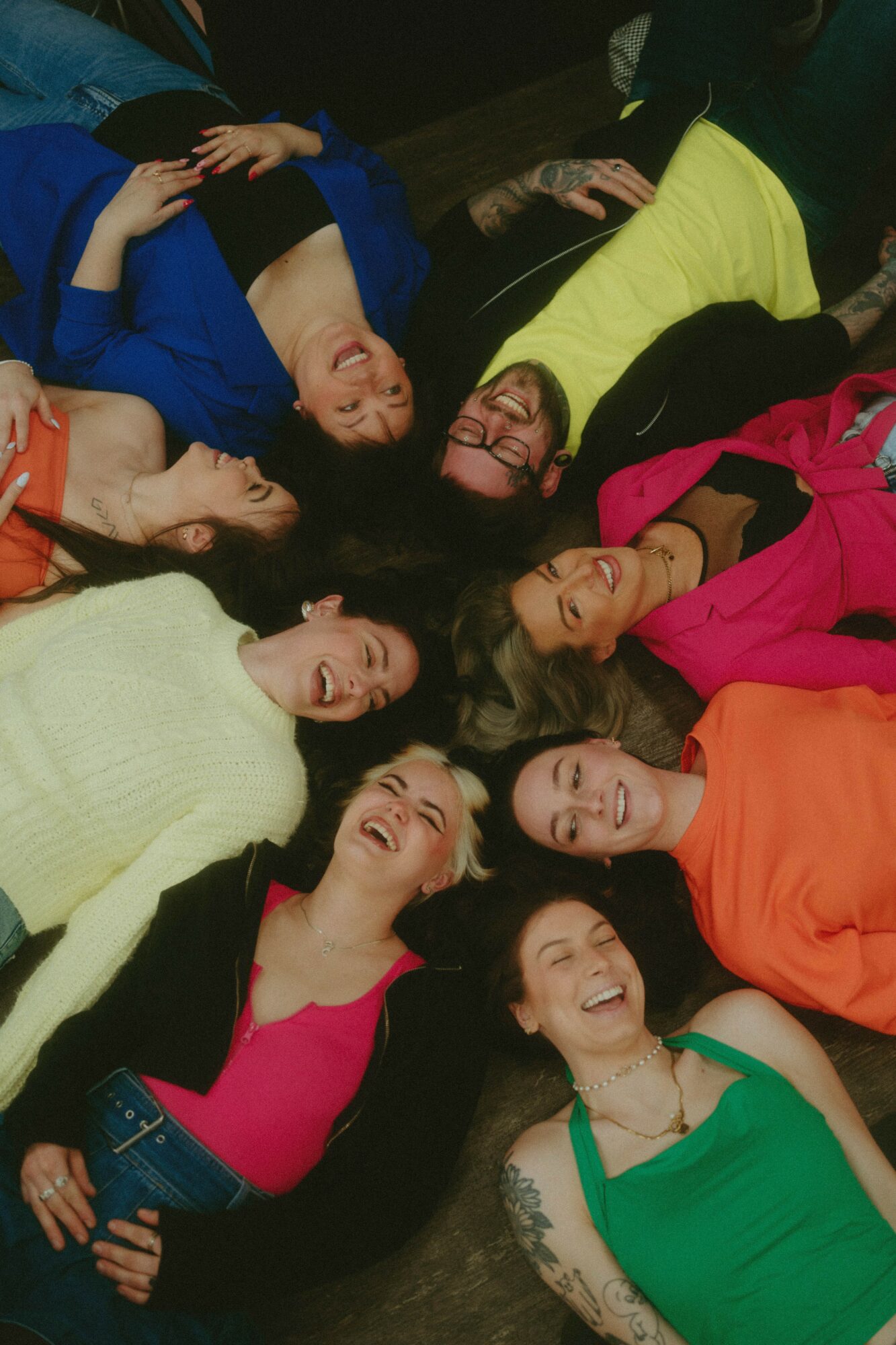 Group of women lying on the floor in a circle, smiling and looking up, wearing colorful clothing.