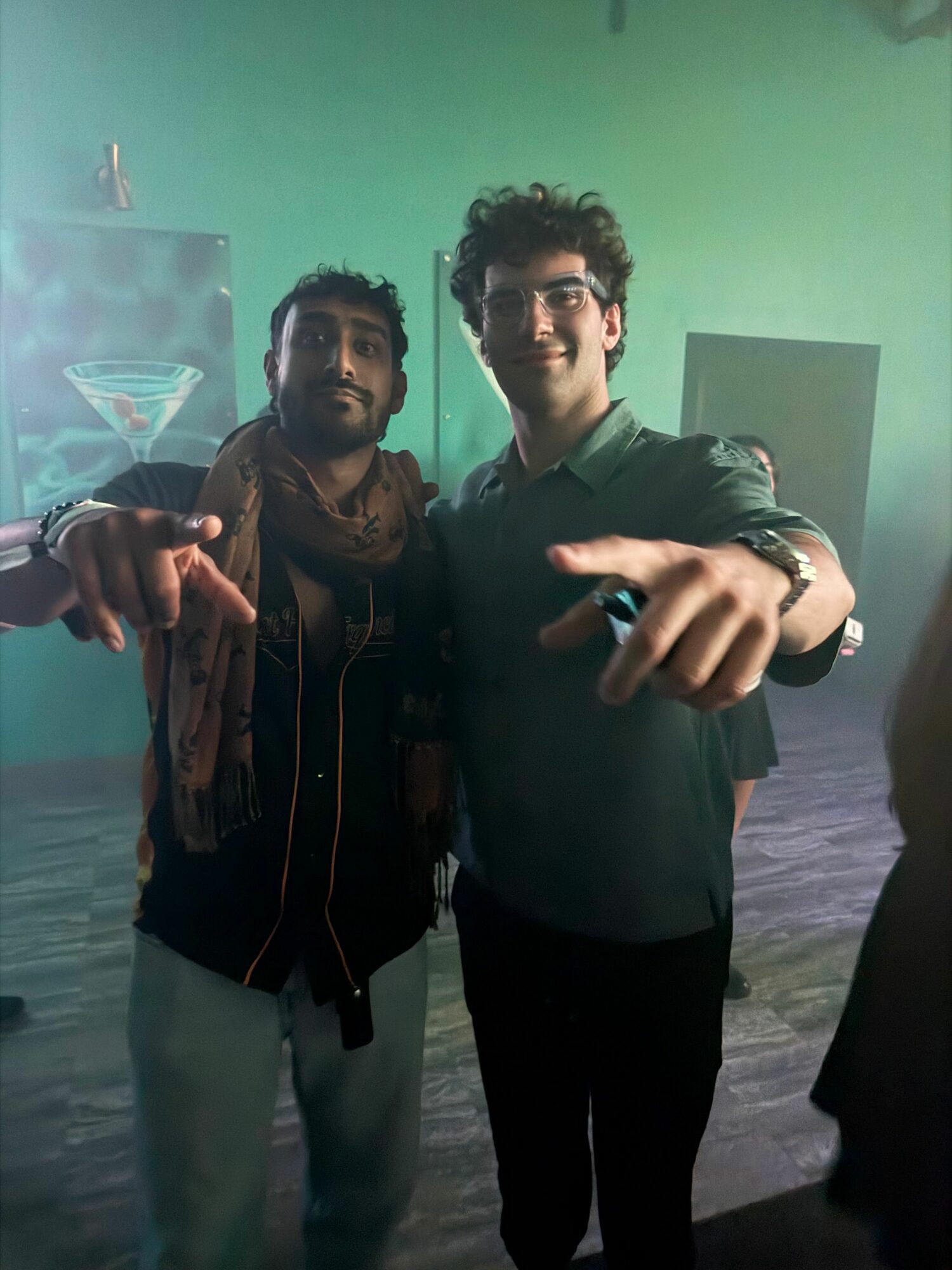 Two people taking a mirror selfie in a room with green and black walls, one making a peace sign.