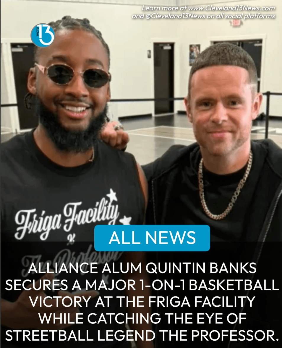 Two men smiling at an indoor event, one wearing sunglasses and a black shirt, the other with short hair and a chain, with a news banner overlay.