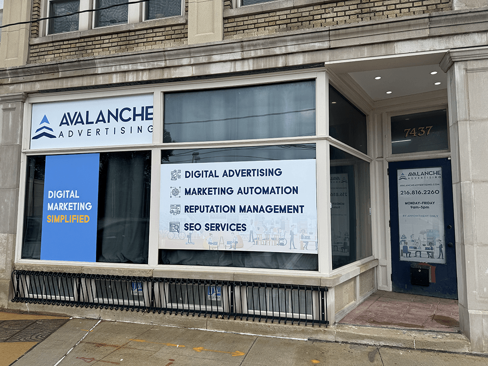 Storefront with Avalanche Advertising sign, large window displaying services, and entrance door, on a city street.