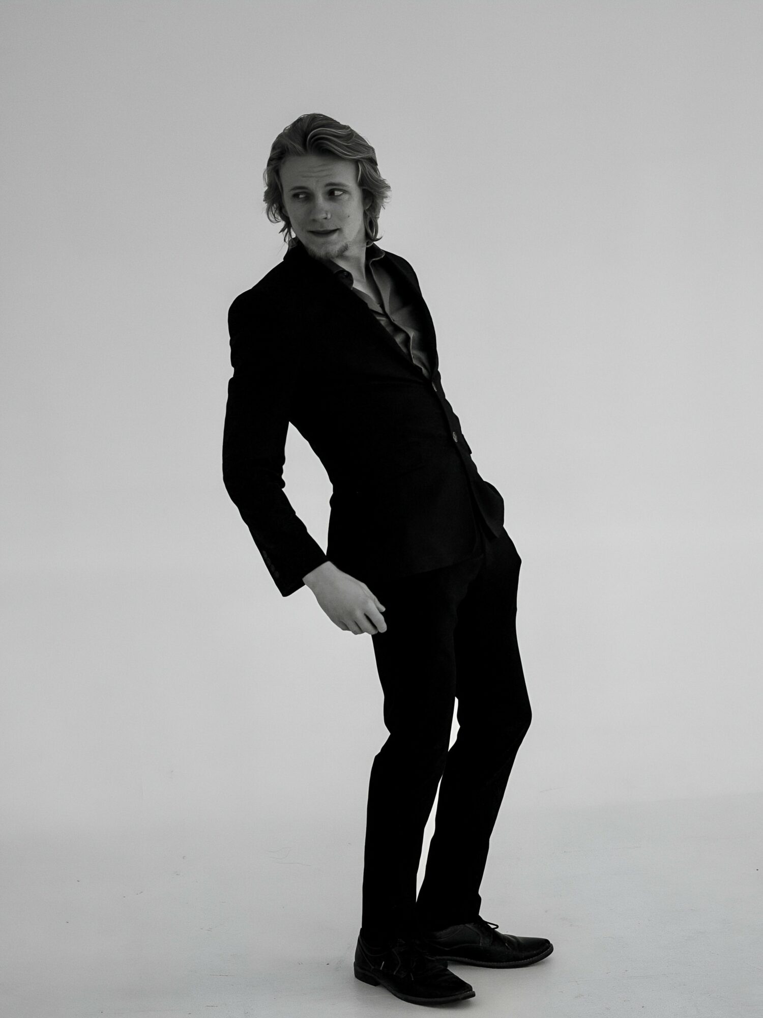 Person in a suit standing with one hand in pocket, looking at camera, against plain background.
