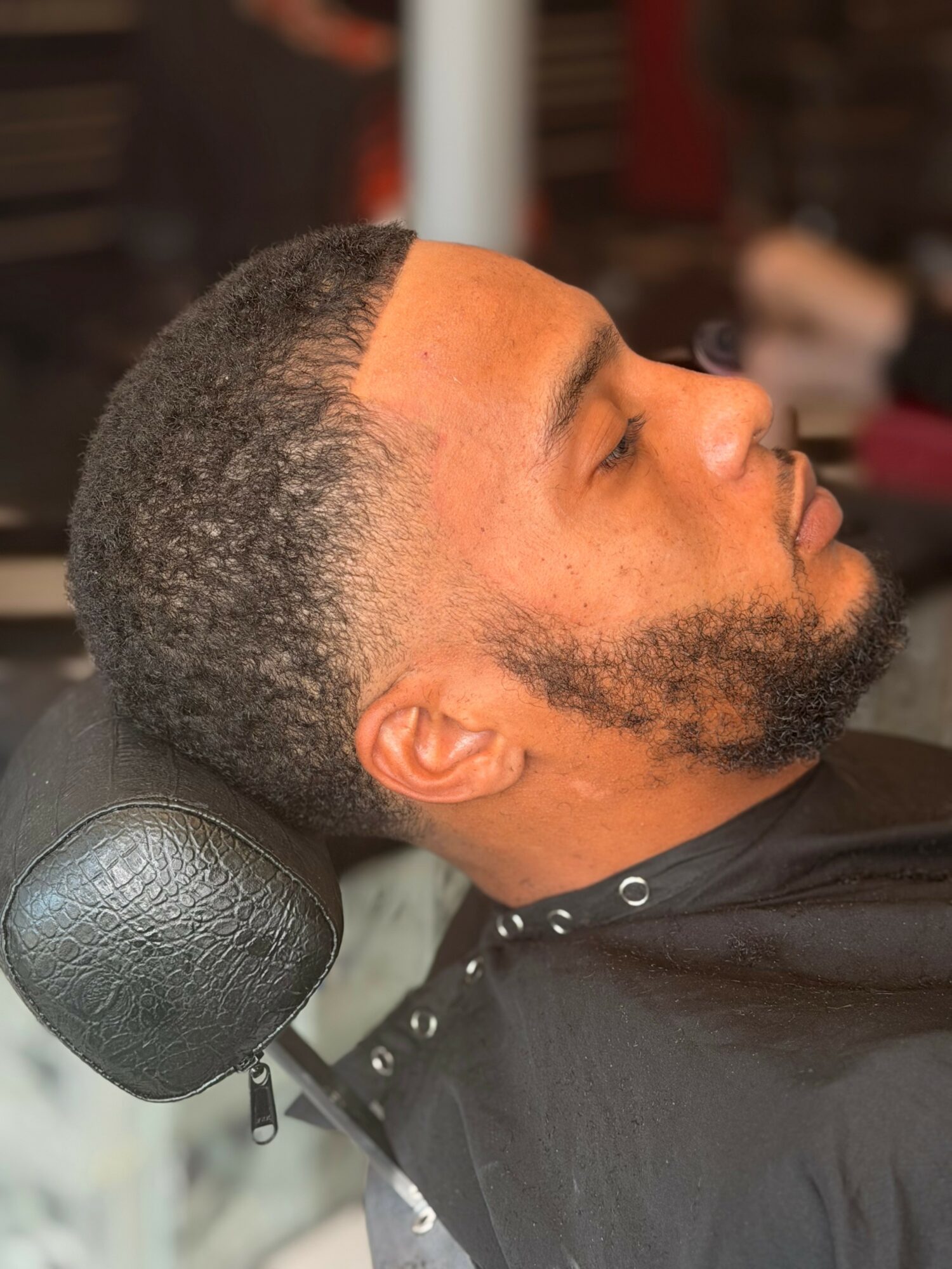 Man with short hair and beard resting with head on a headrest in a salon chair.