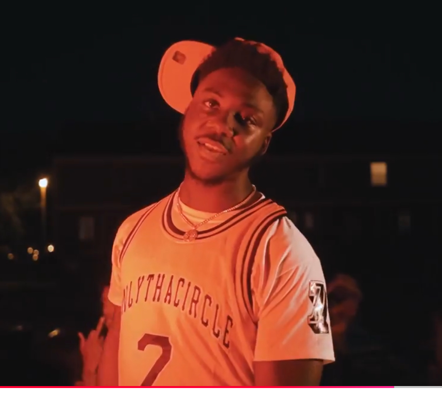 Young man wearing a baseball cap backwards and a sports jersey, standing outdoors at night.