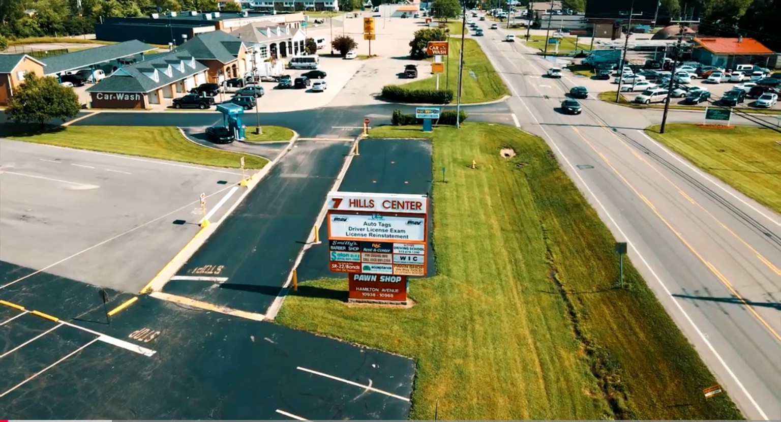 A parking lot with a sign for Hills Center and a grassy area, viewed from above during daytime.