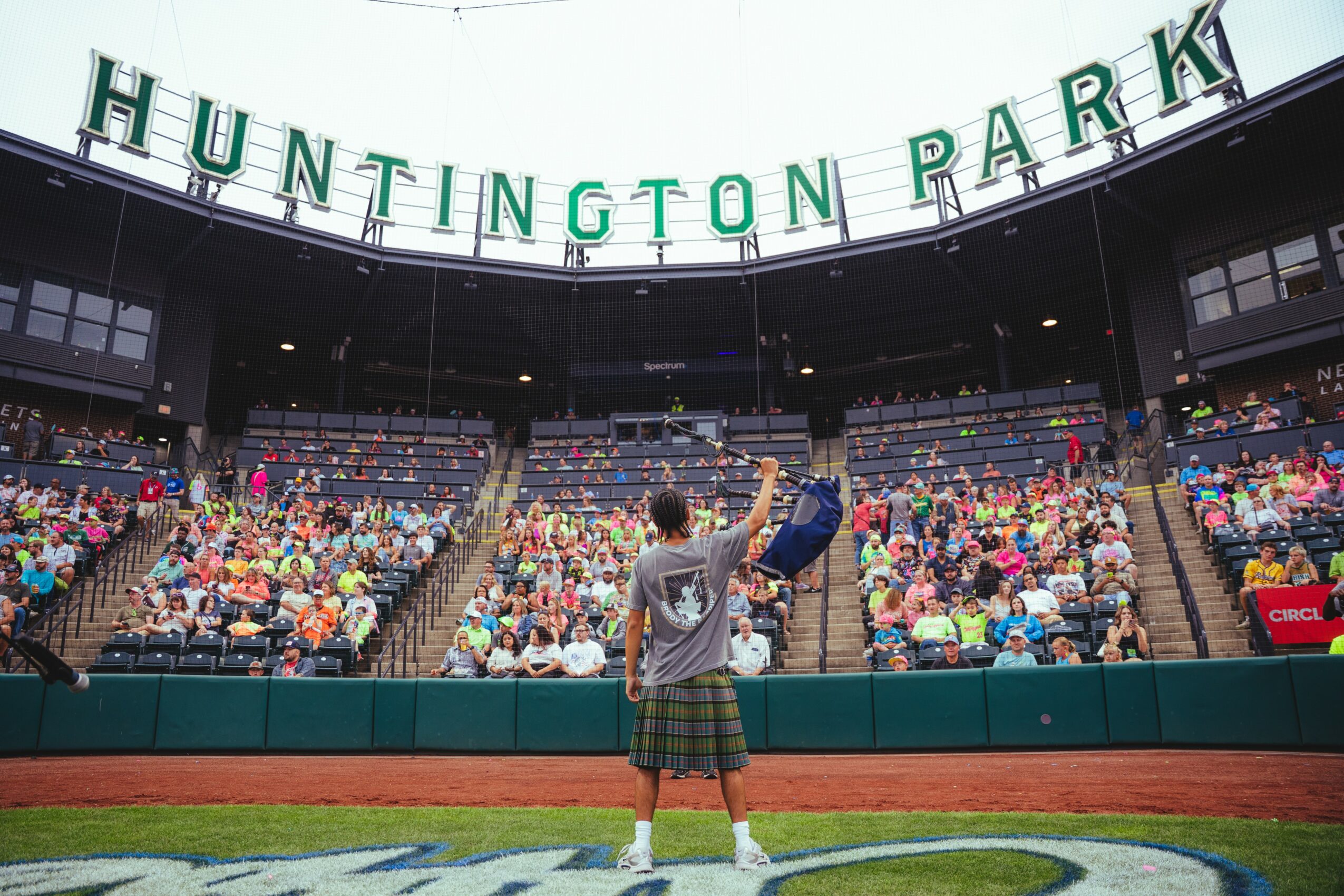 Child standing on field with glove, facing audience in stadium, Huntington Park sign overhead, crowd seated in stands.