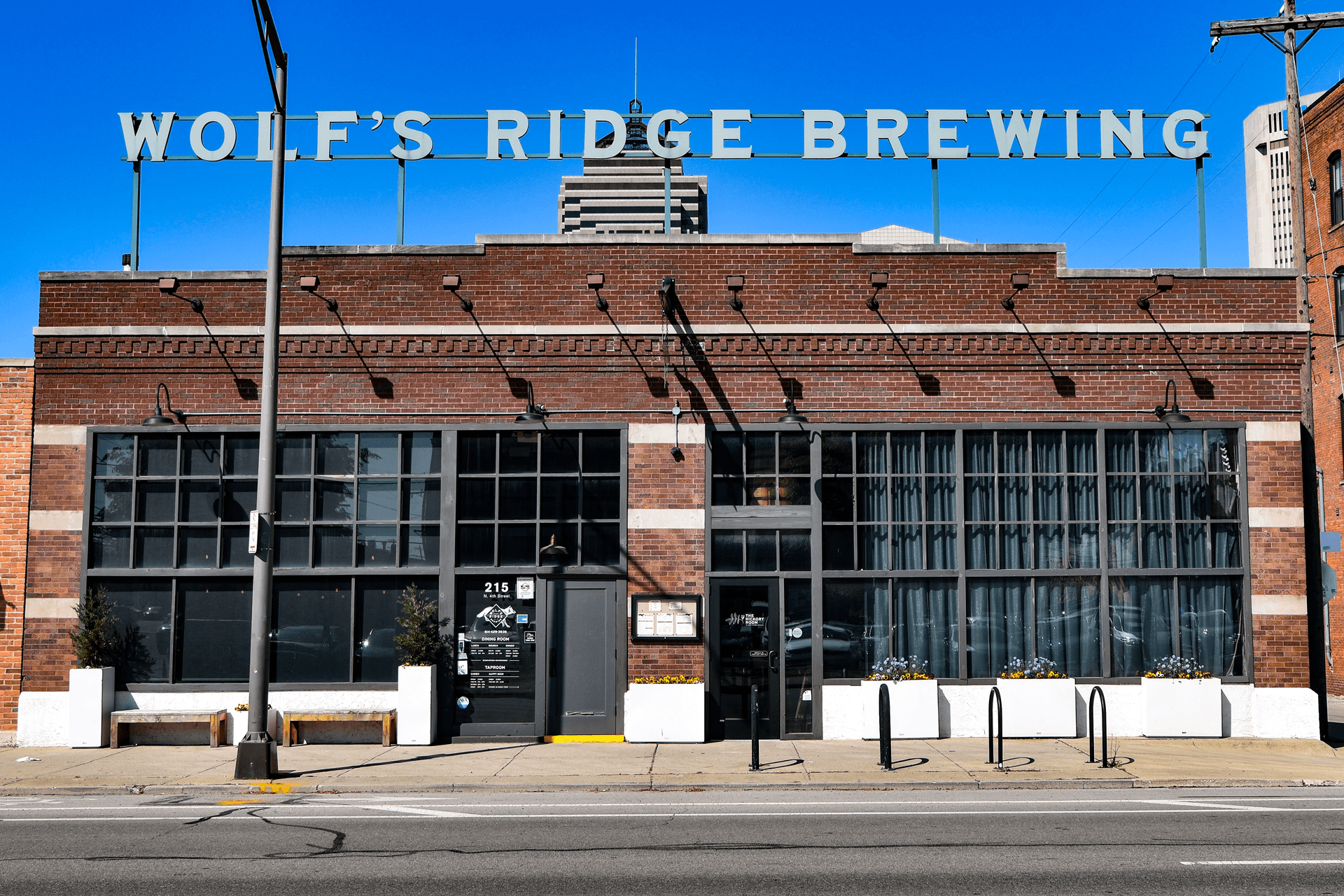 Brick building with large windows and a sign reading 'WOLF'S RIDGE BREWING' on top, under a clear blue sky.