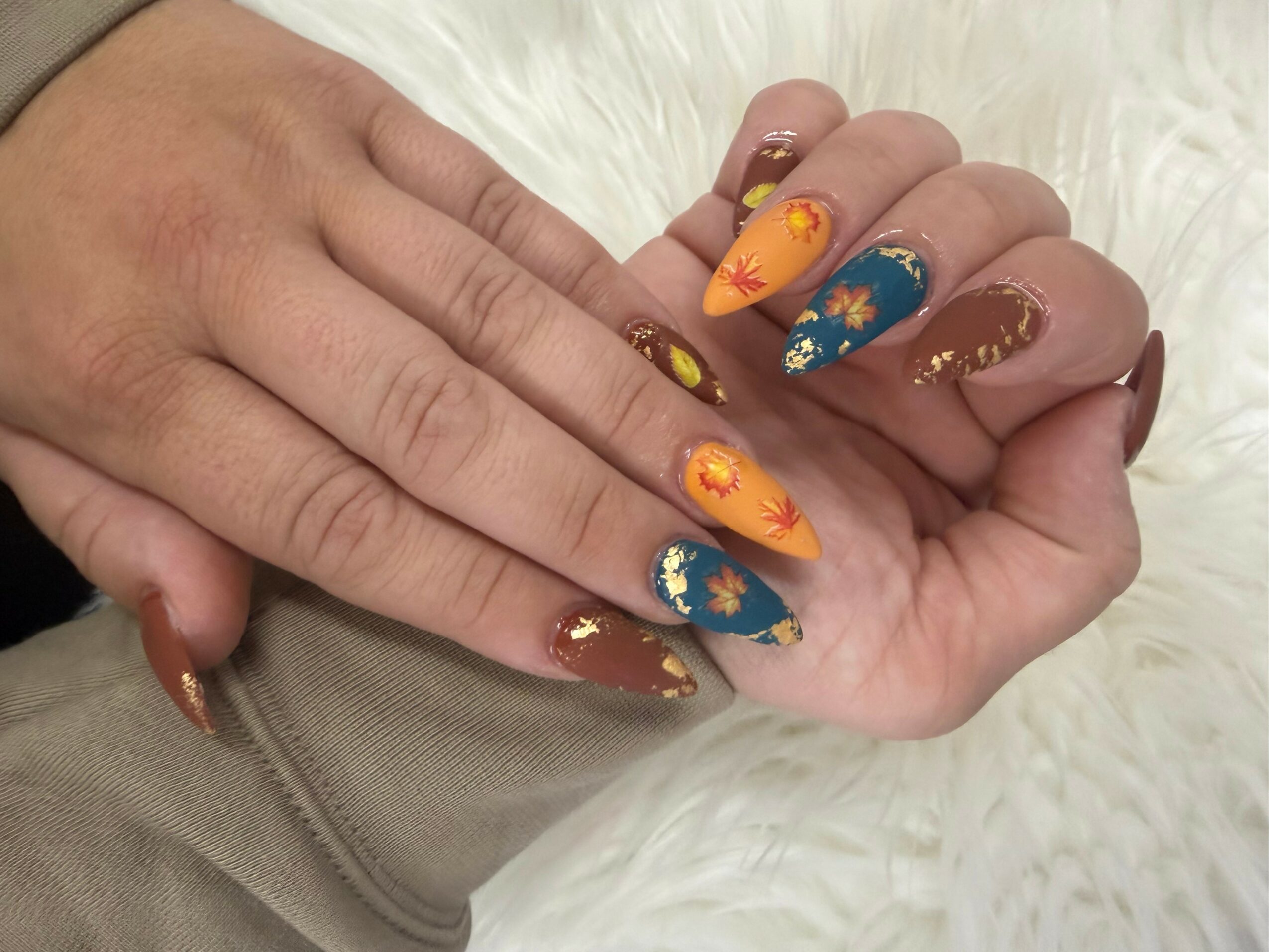 Hands with colorful floral and decorative nail art, resting on a soft, white surface.