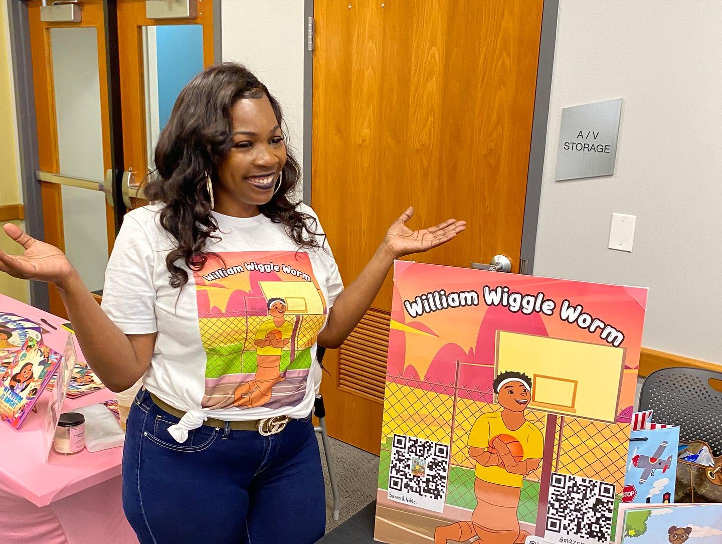 Woman smiling and gesturing next to a colorful display board with a cartoon character and QR codes.