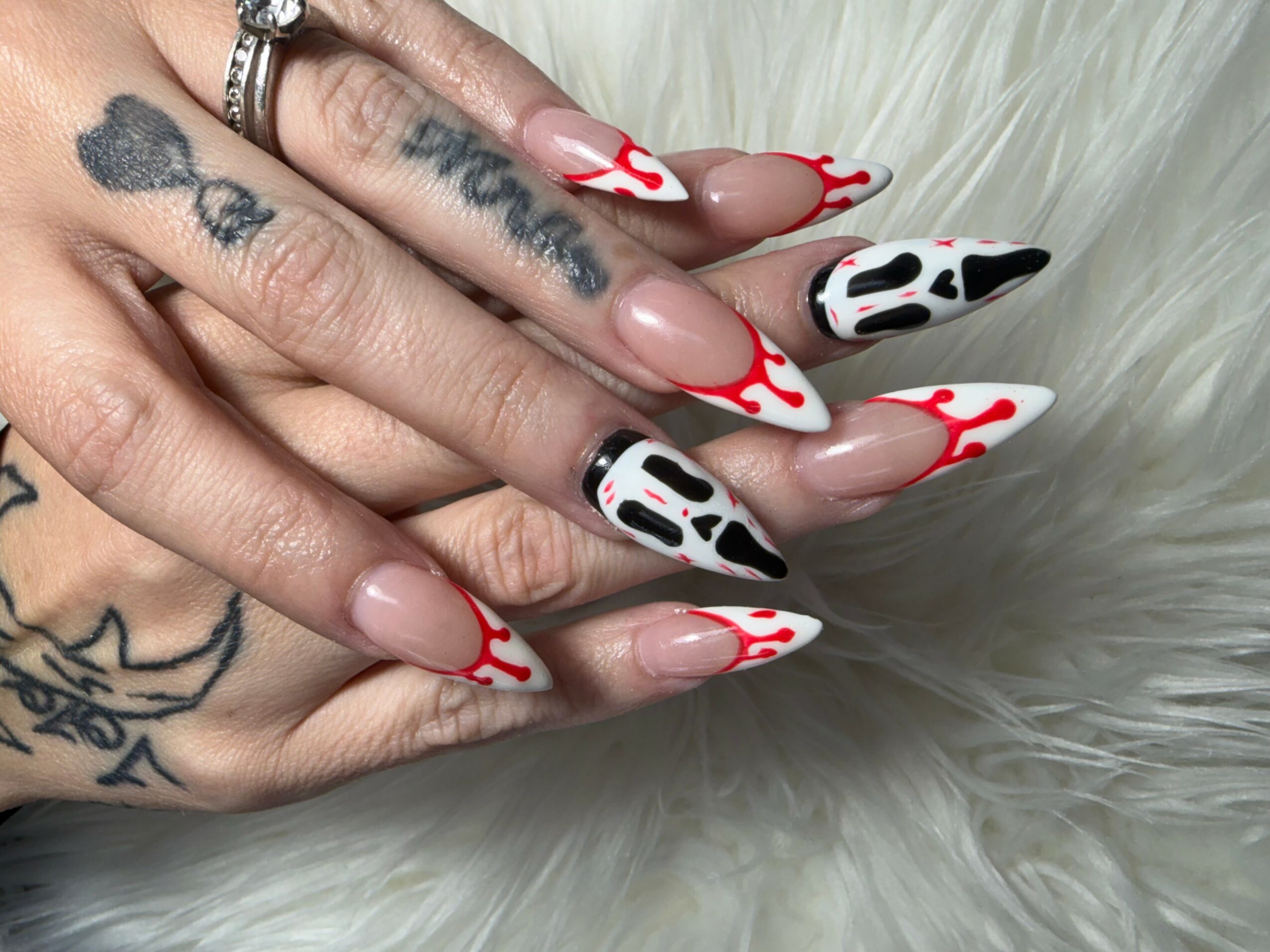 Hands with tattoos and long nails resting on a furry surface, featuring cow print and red flame nail designs.