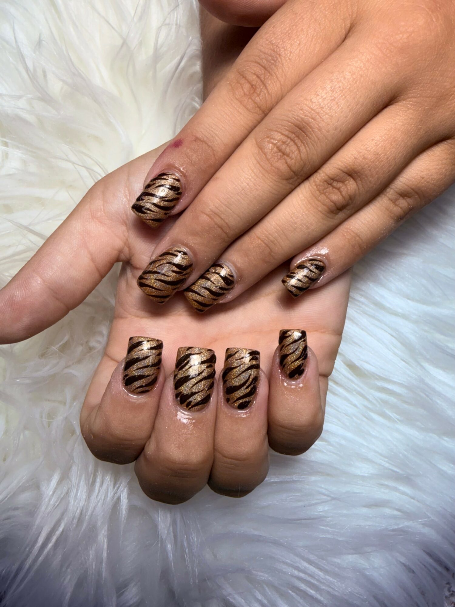 Hands with tiger stripe patterned nail art, resting on a white furry surface.